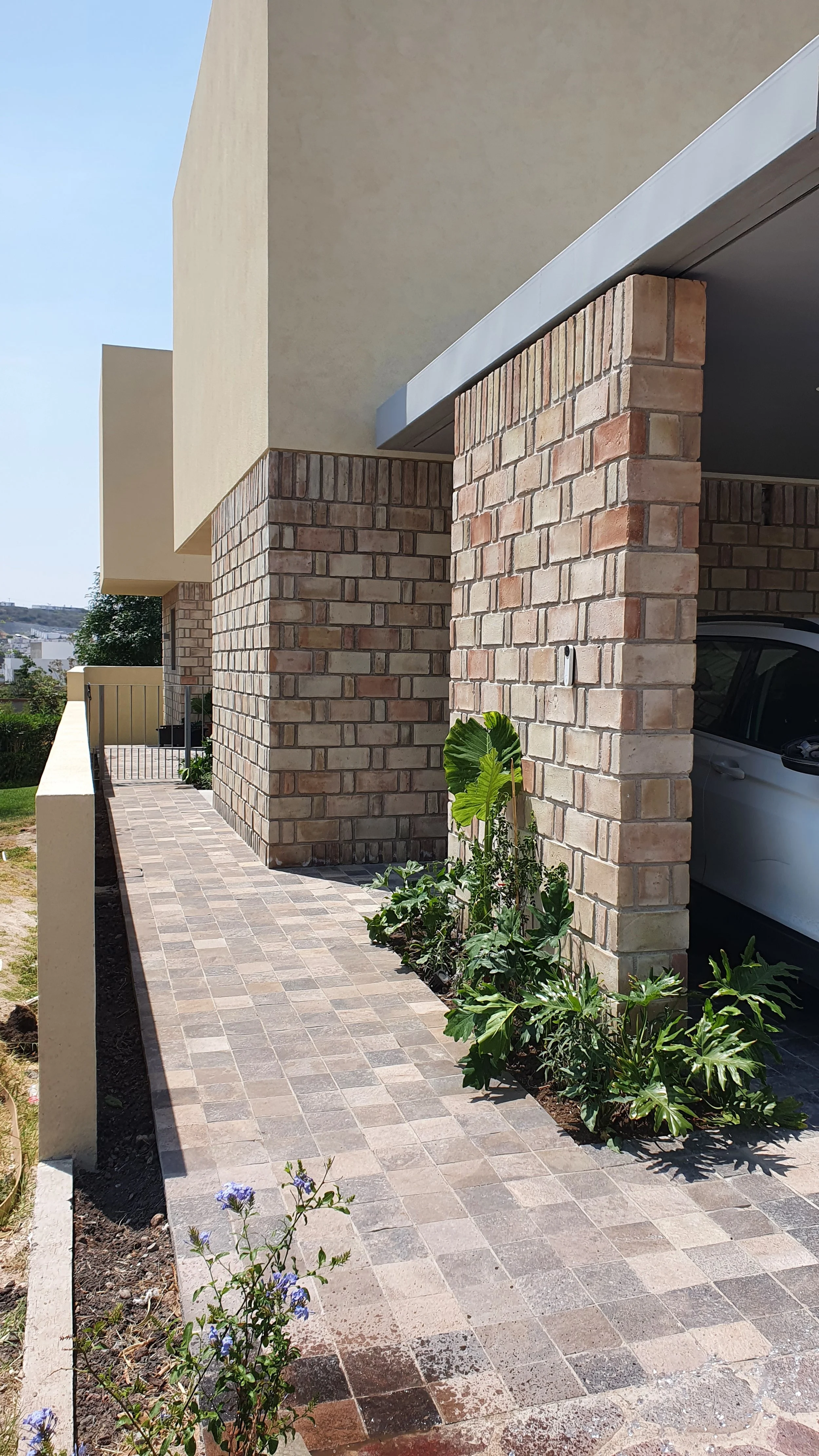 Camino de ladrillos junto a una casa de ladrillos con plantas verdes y un auto en el garaje