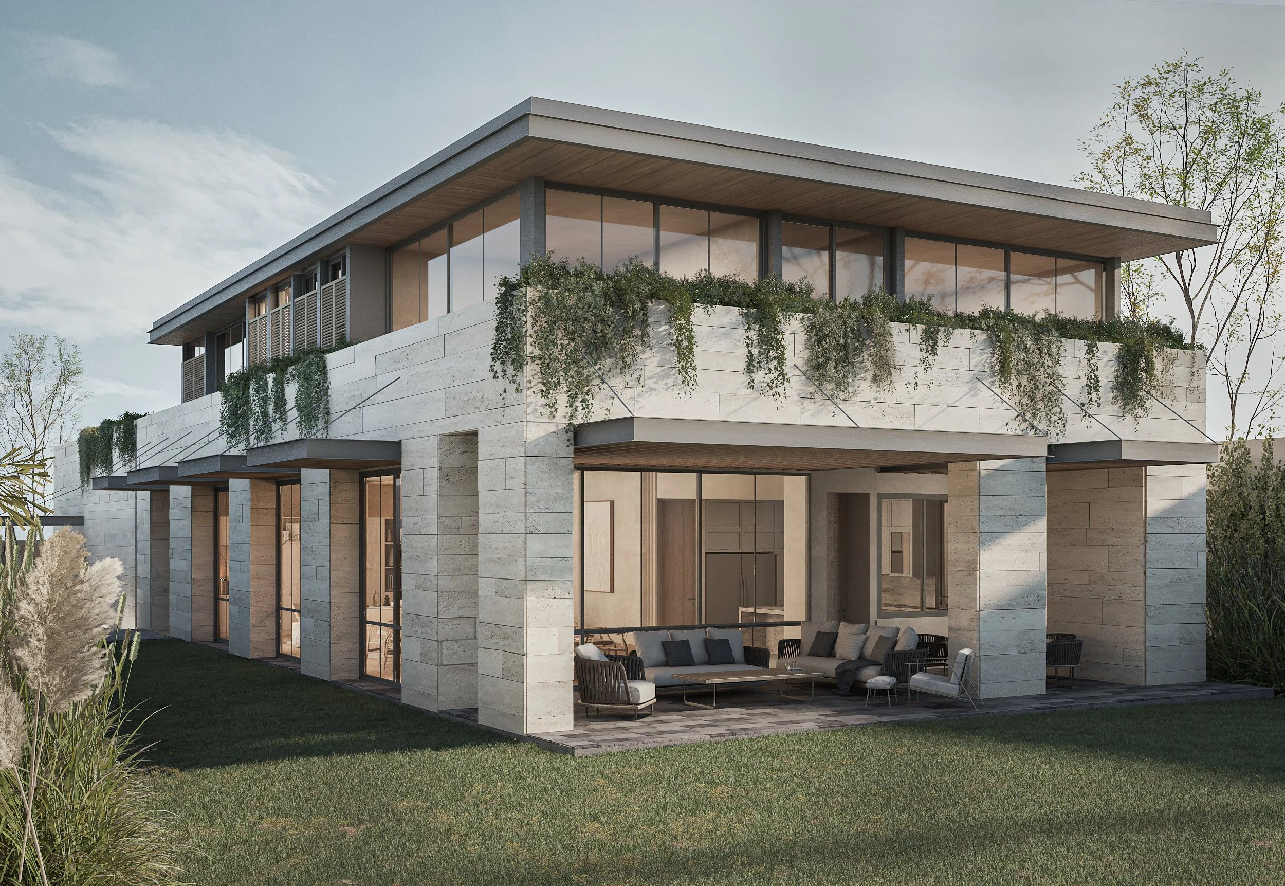 Una casa moderna de dos pisos con paredes de piedra y varias ventanas grandes, con una terraza en la planta baja y un balcón en la planta superior con plantas colgantes, rodeada de césped y árboles.