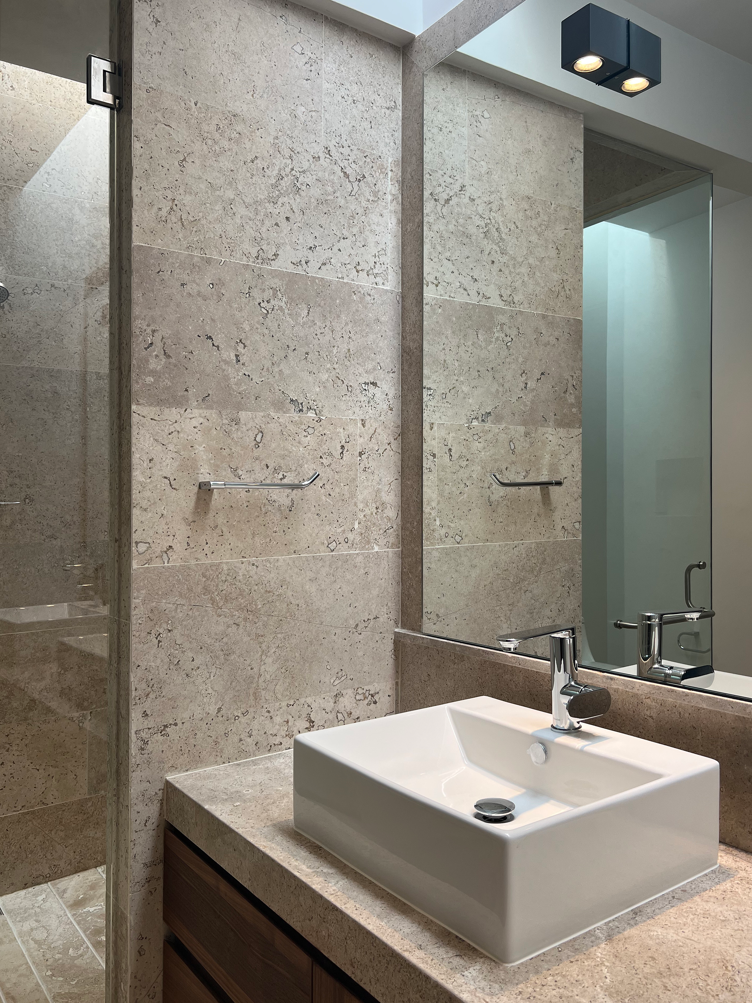 Lavabo rectangular de cerámica blanca con grifo moderno en un baño con paredes de piedra y un gran espejo.
