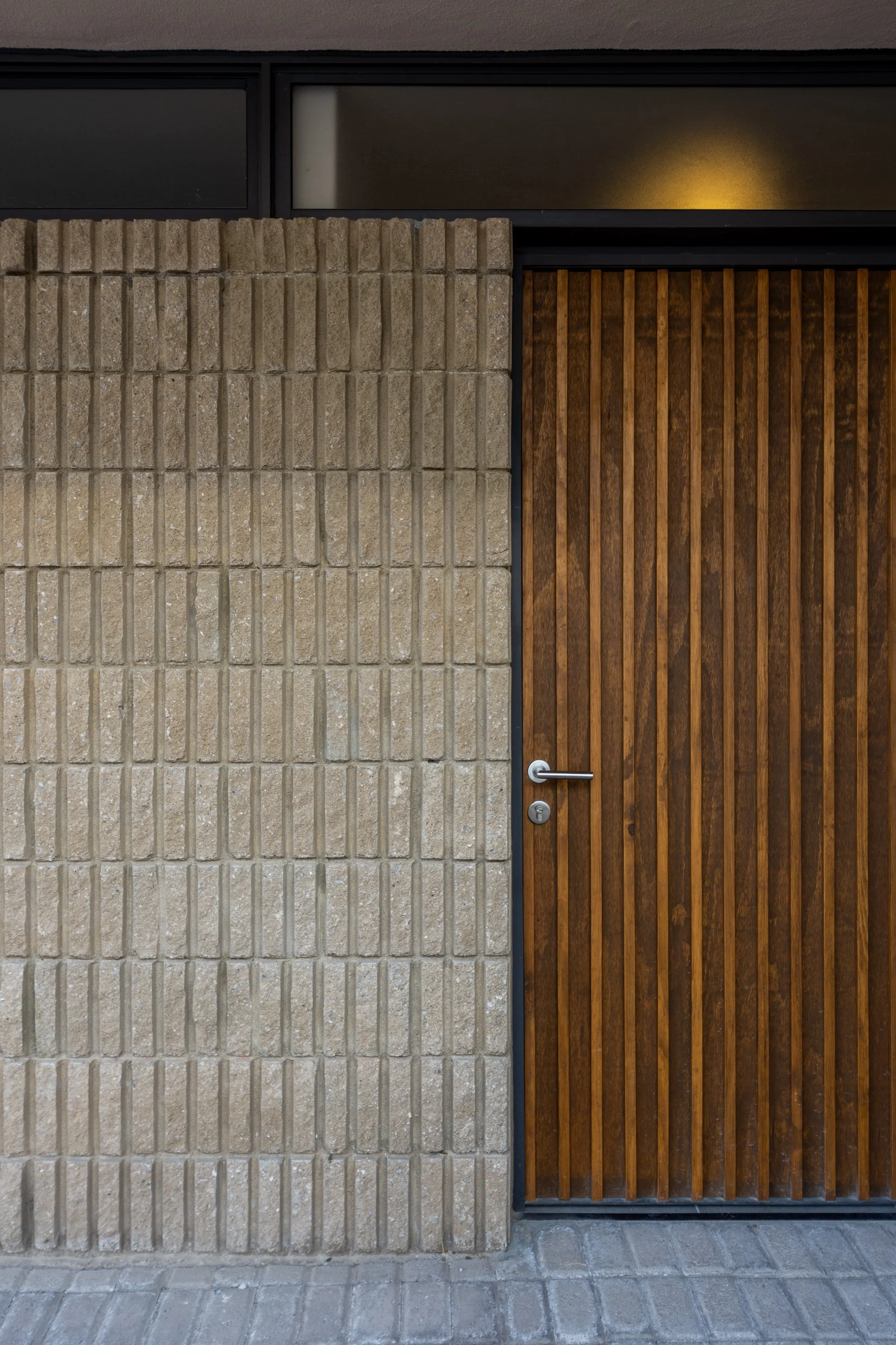 Puerta de madera con barras verticales enmarcada por una pared de bloques de cemento y una ventana con vidrio en la parte superior.