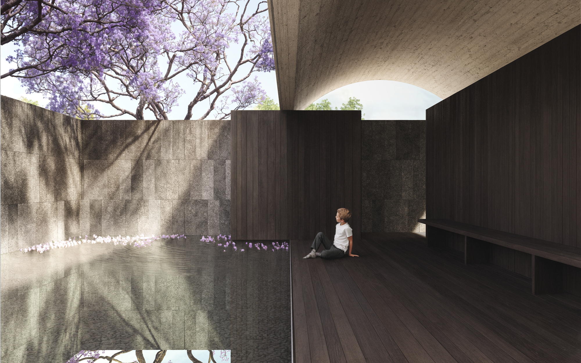 Un niño sentado en una estructura moderna de madera y concreto, con una pared de piedra y árboles con flores lilas al fondo.
