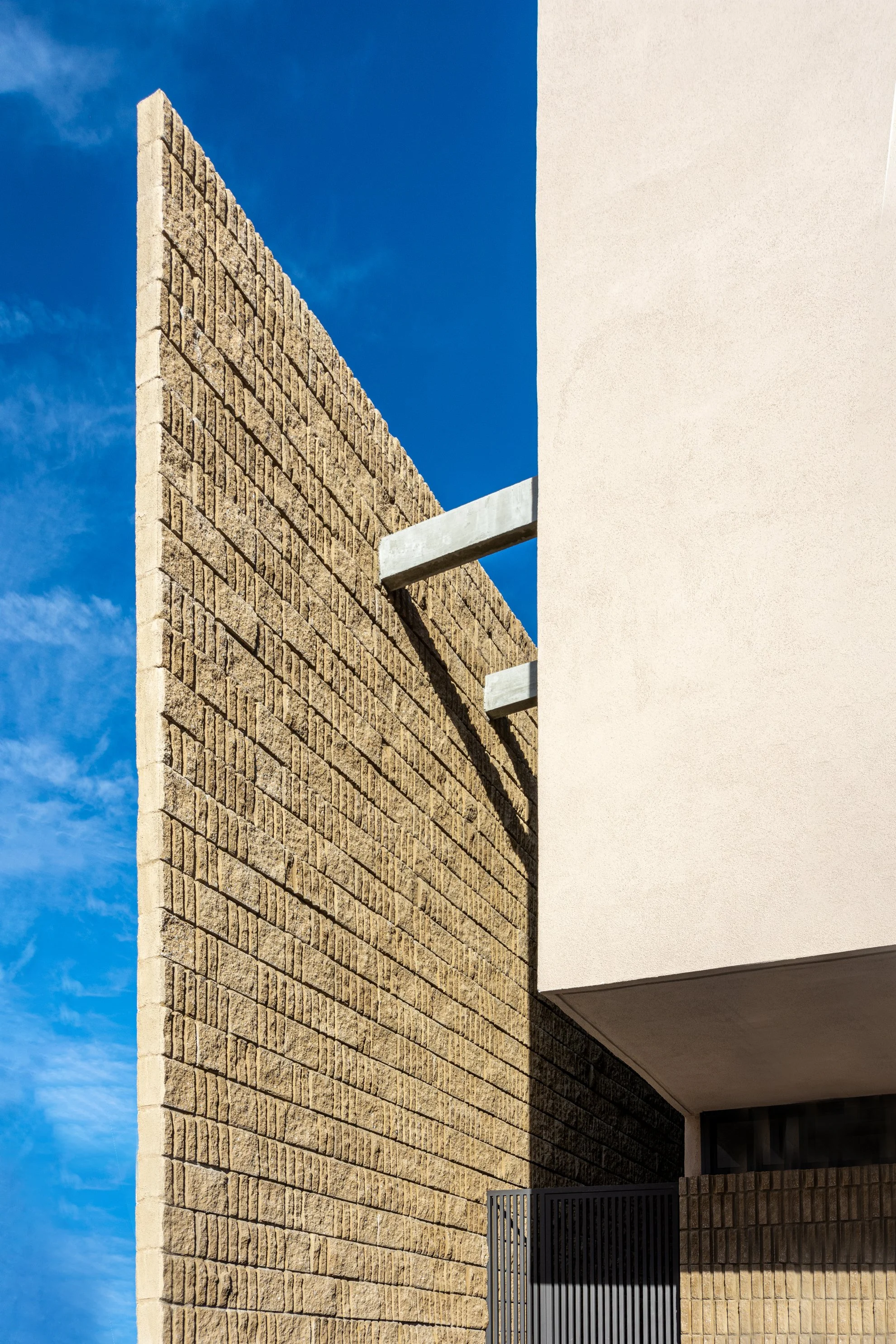 Vista de un edificio moderno con paredes de ladrillos y una parte de la estructura de concreto, bajo un cielo azul con algunas nubes.