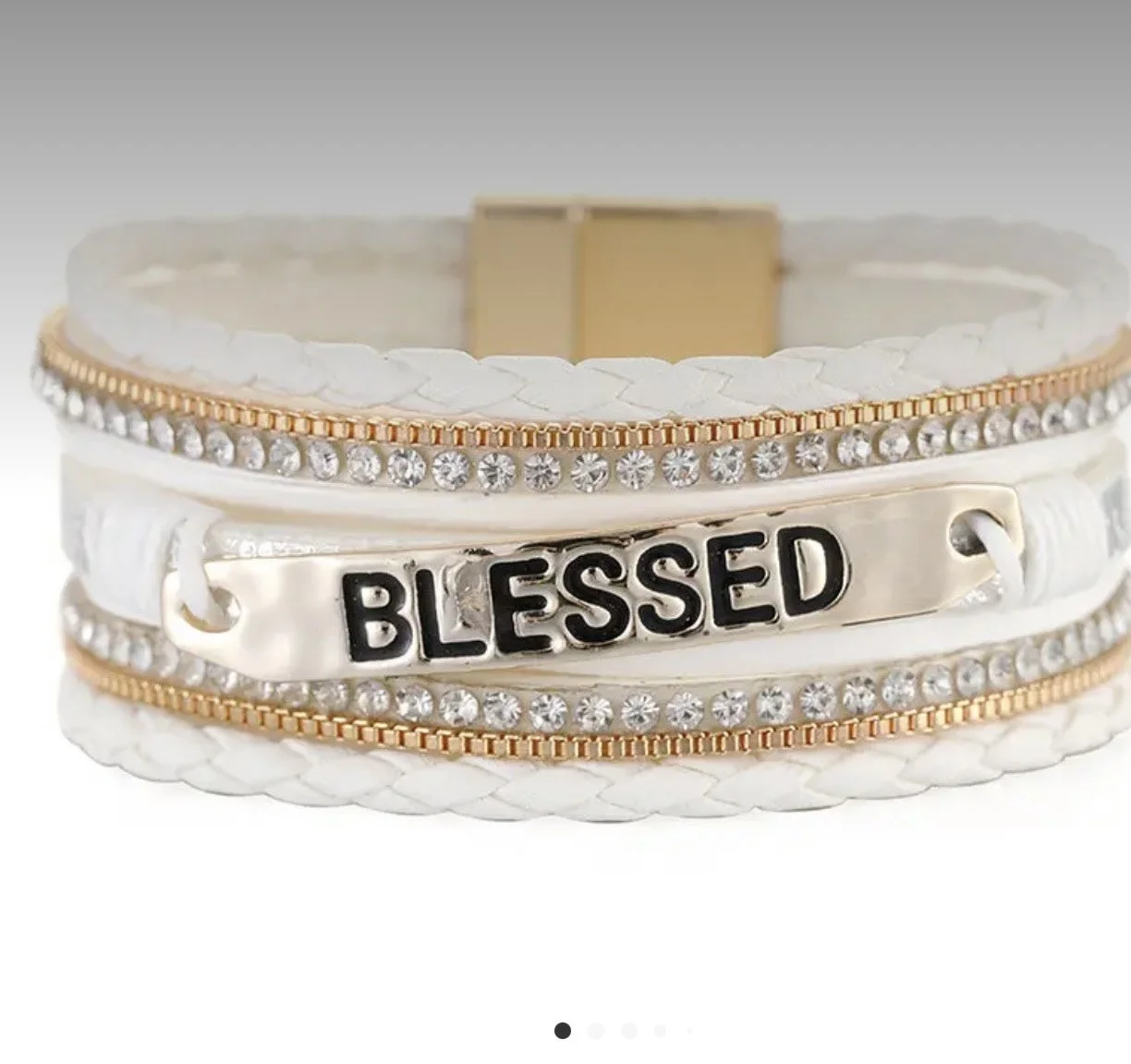 A layered bracelet with white braided bands, rhinestones, and a metal plate that says 'BLESSED' in black letters.