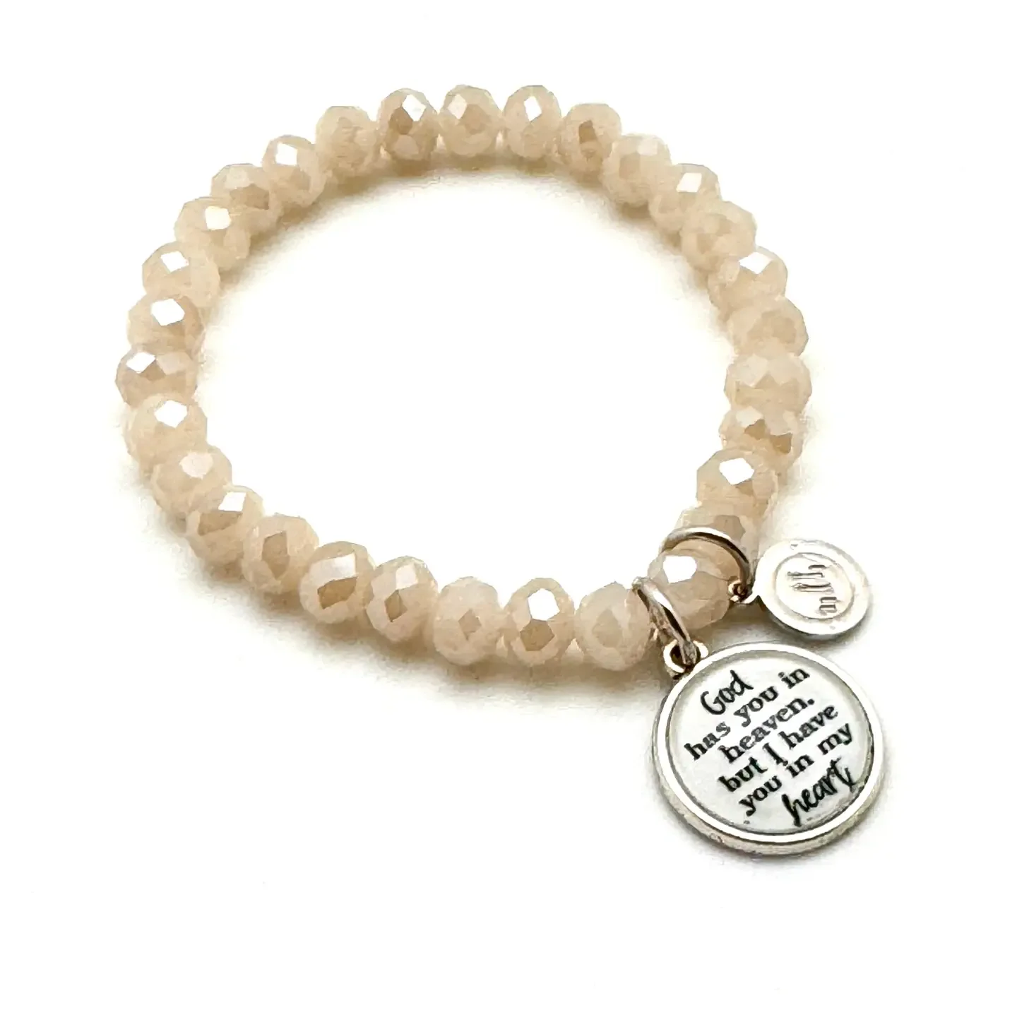Beige beaded bracelet with two circular charms, one engraved with the message, "God has you in heaven, but I have you in my heart."
