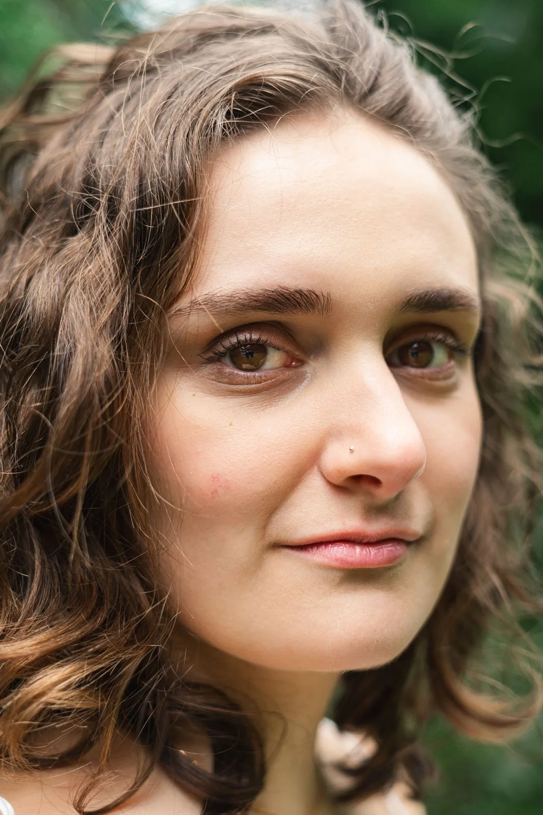 Retrato de uma mulher com cabelo cacheado e olhos castanhos em ambiente natural.