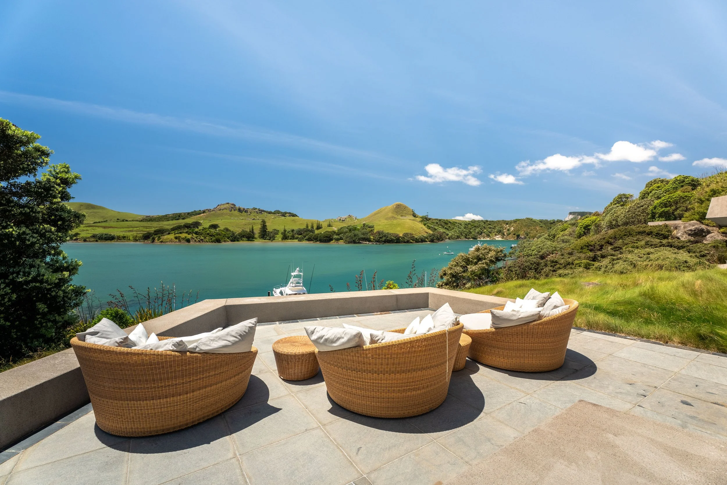 Patio with wicker chairs and pillows overlooking a lake with green hills and blue sky