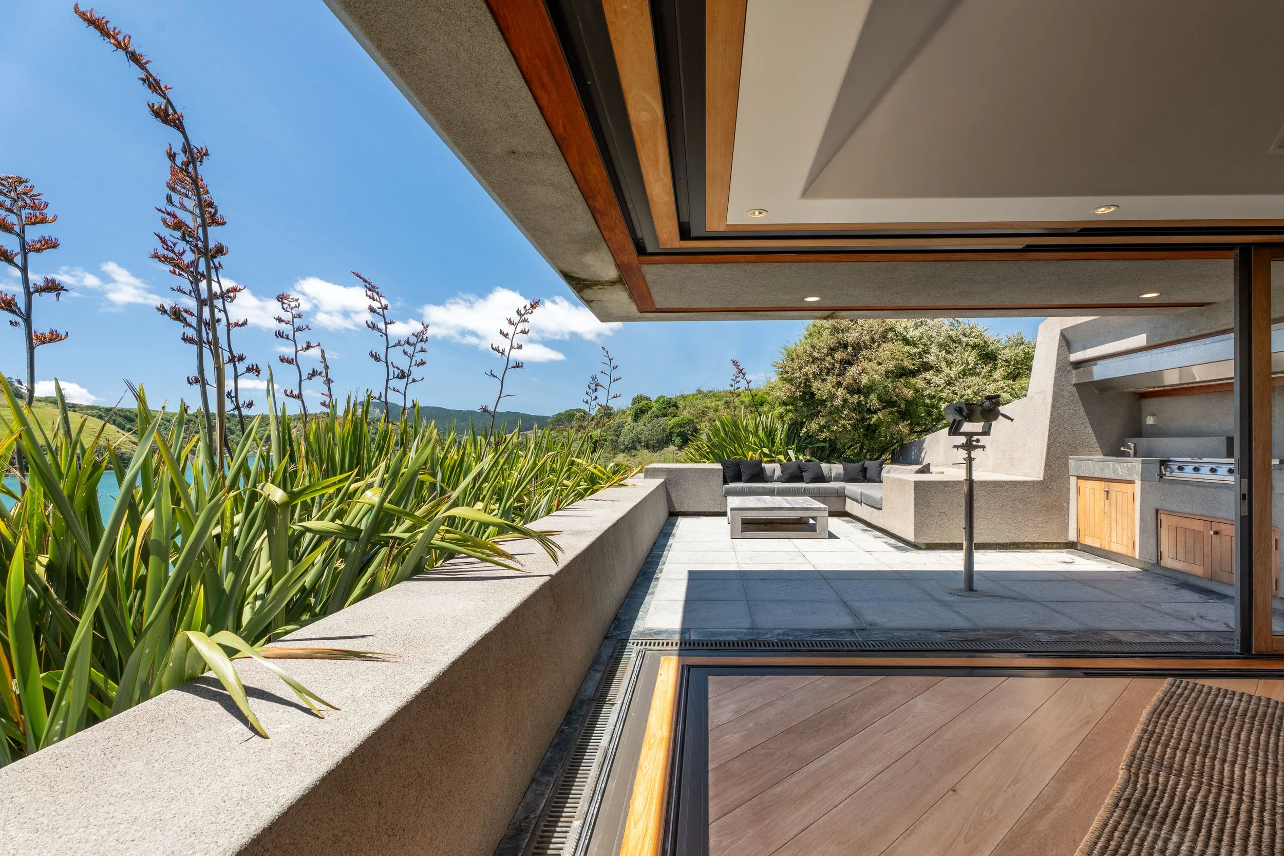 Modern outdoor patio with built-in outdoor kitchen, lounge seating, and scenic view of greenery and blue sky.