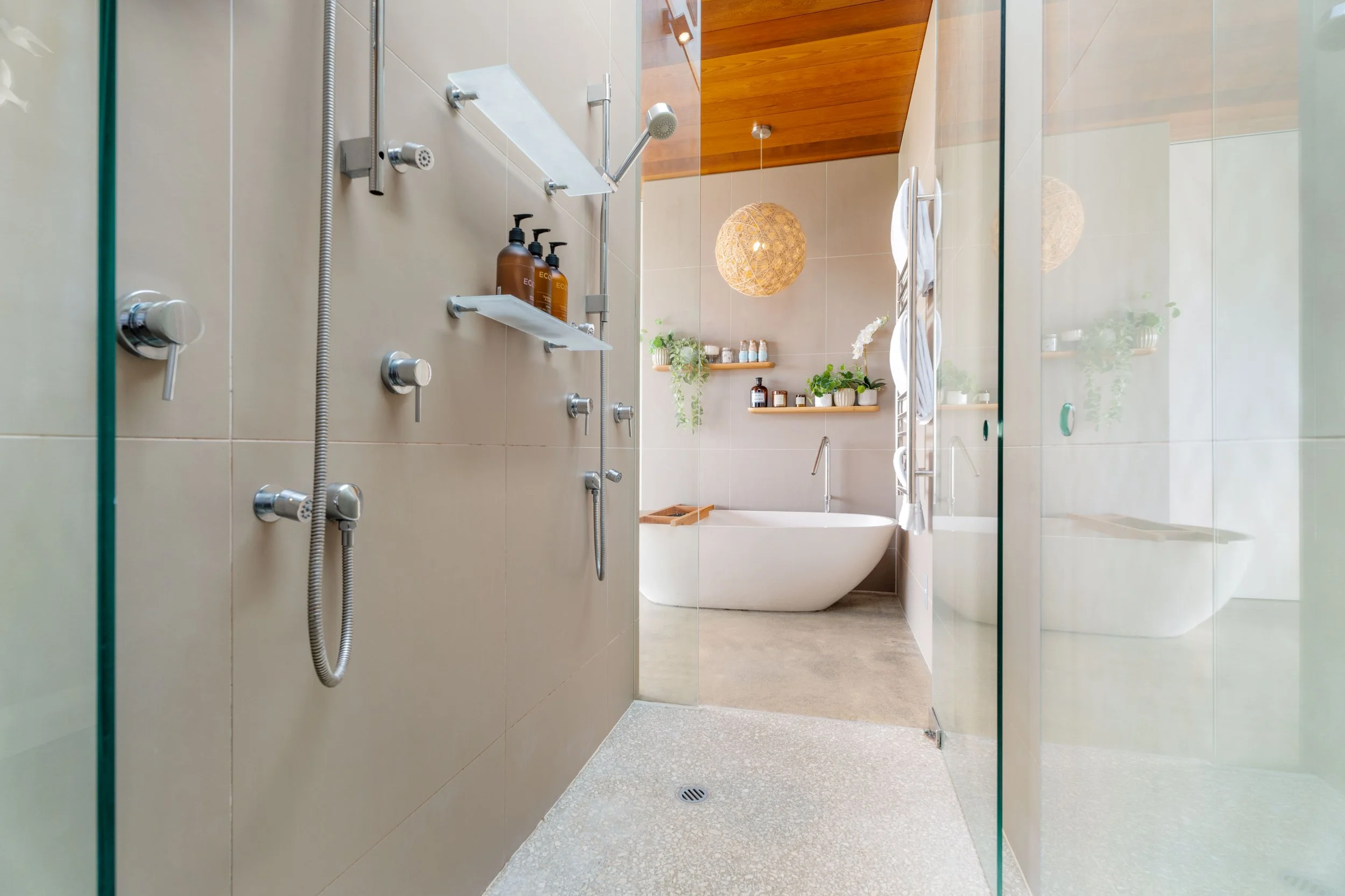Modern bathroom with a walk-in shower, glass partition, and bathtub, decorated with plants and wooden accents.