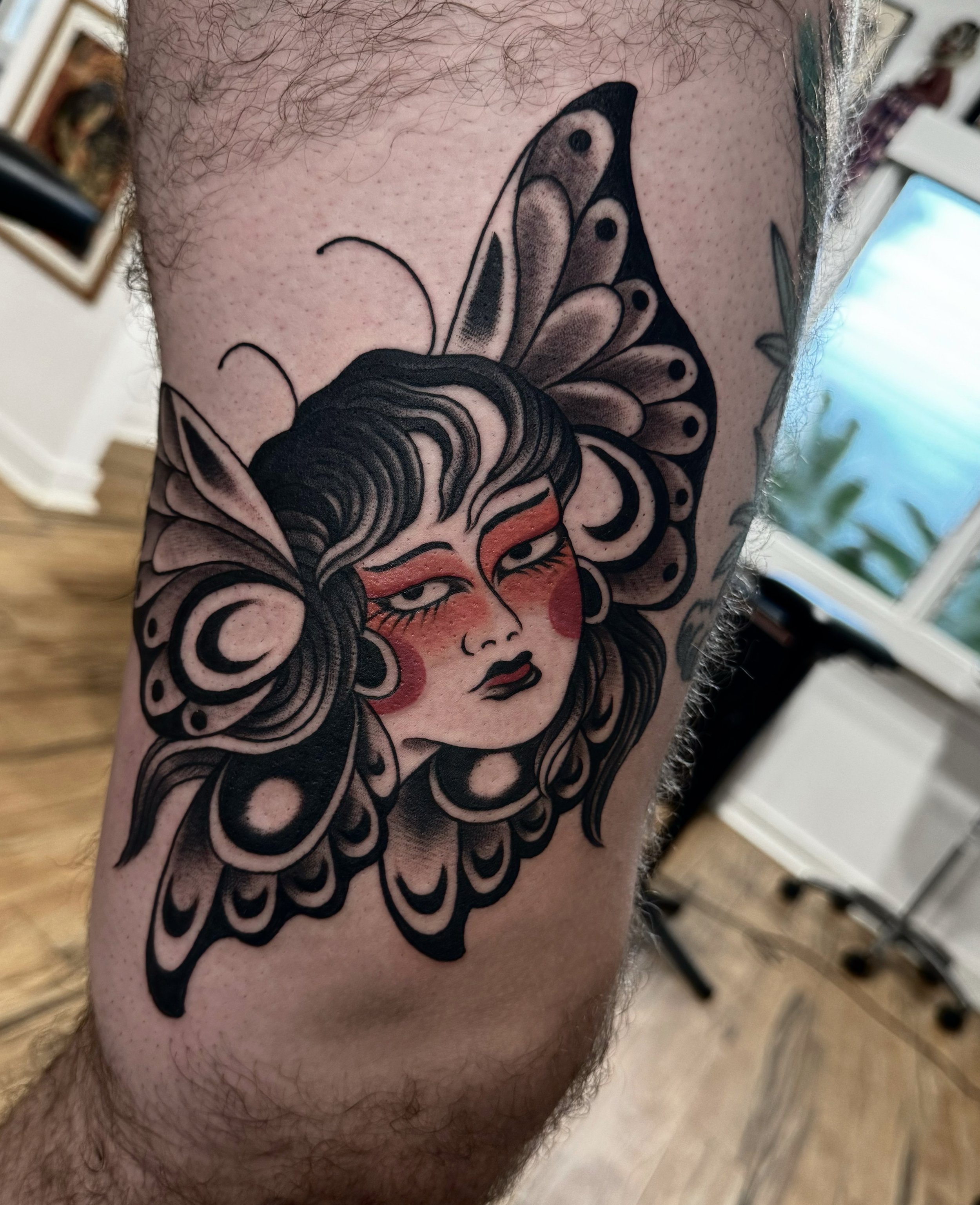 Tattoo of a woman with butterfly wings on her head, styled in traditional tattoo art, with makeup and earrings.