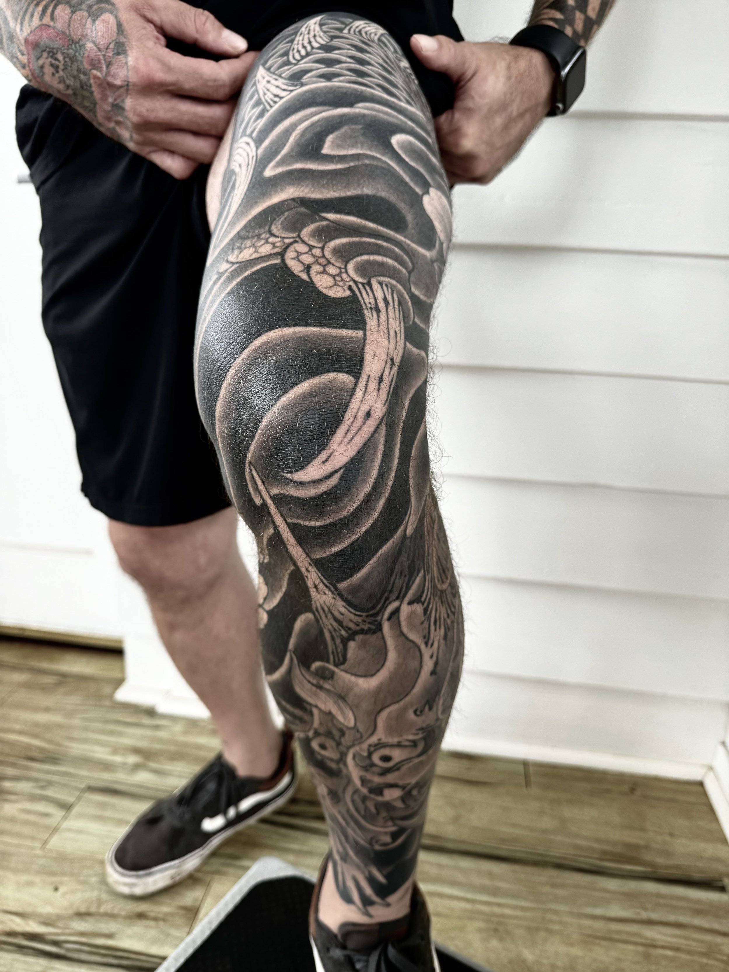 A person with heavily tattooed leg, showing a large black and gray tattoo of a snake, with a hand adjusting the shorts.