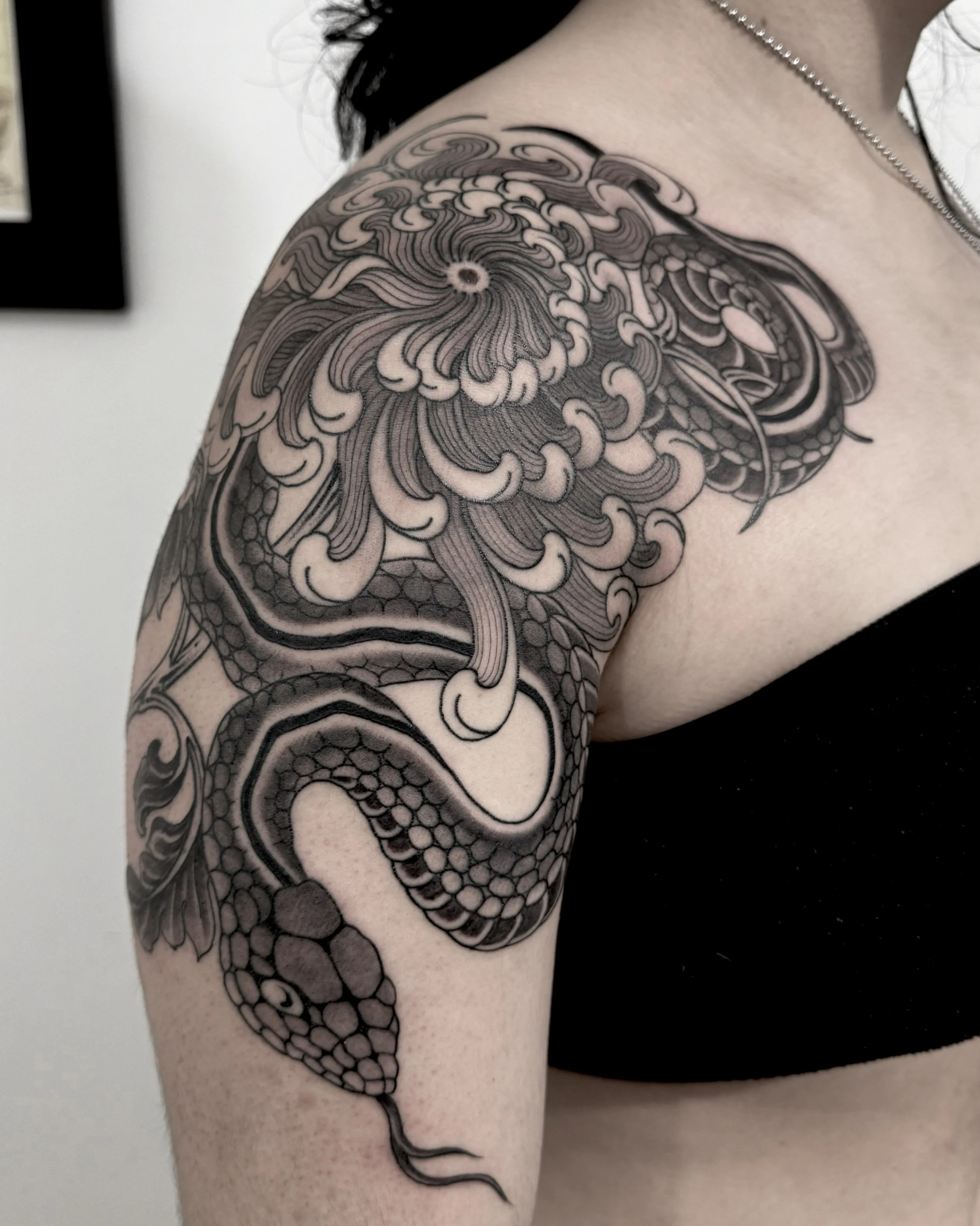Black and gray tattoo of a dragon on a person's upper arm and shoulder.