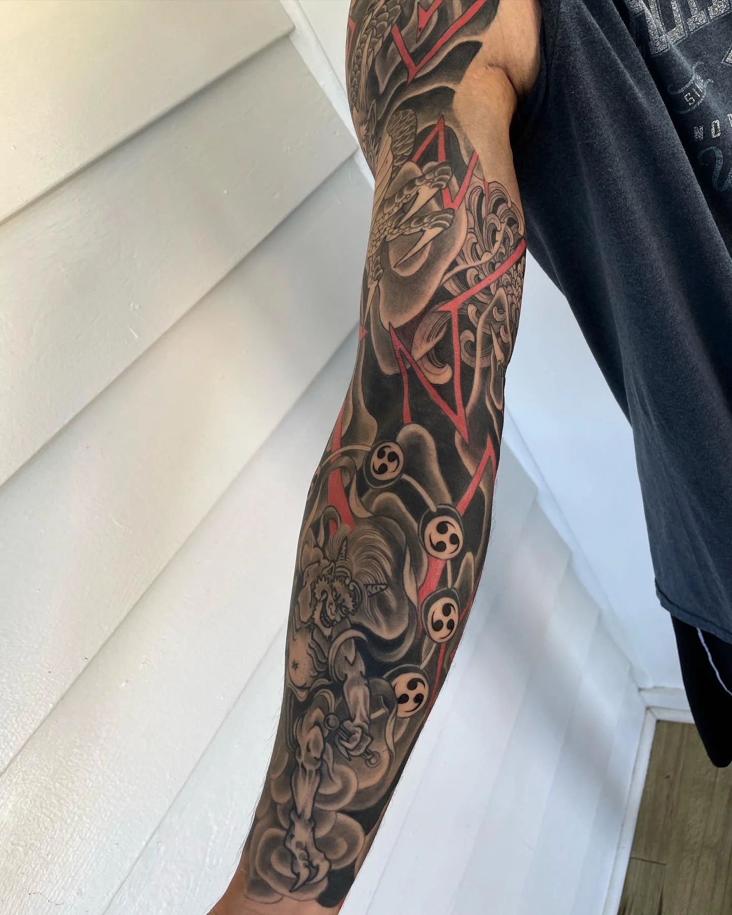 A black and red tattoo sleeve featuring a dragon, a demon, and symbols on a person's arm.