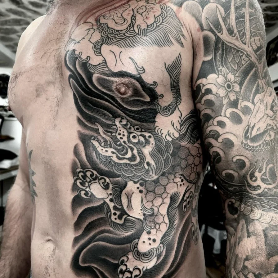Black and gray tattoo of a traditional Japanese style dragon on a man's chest and arm.