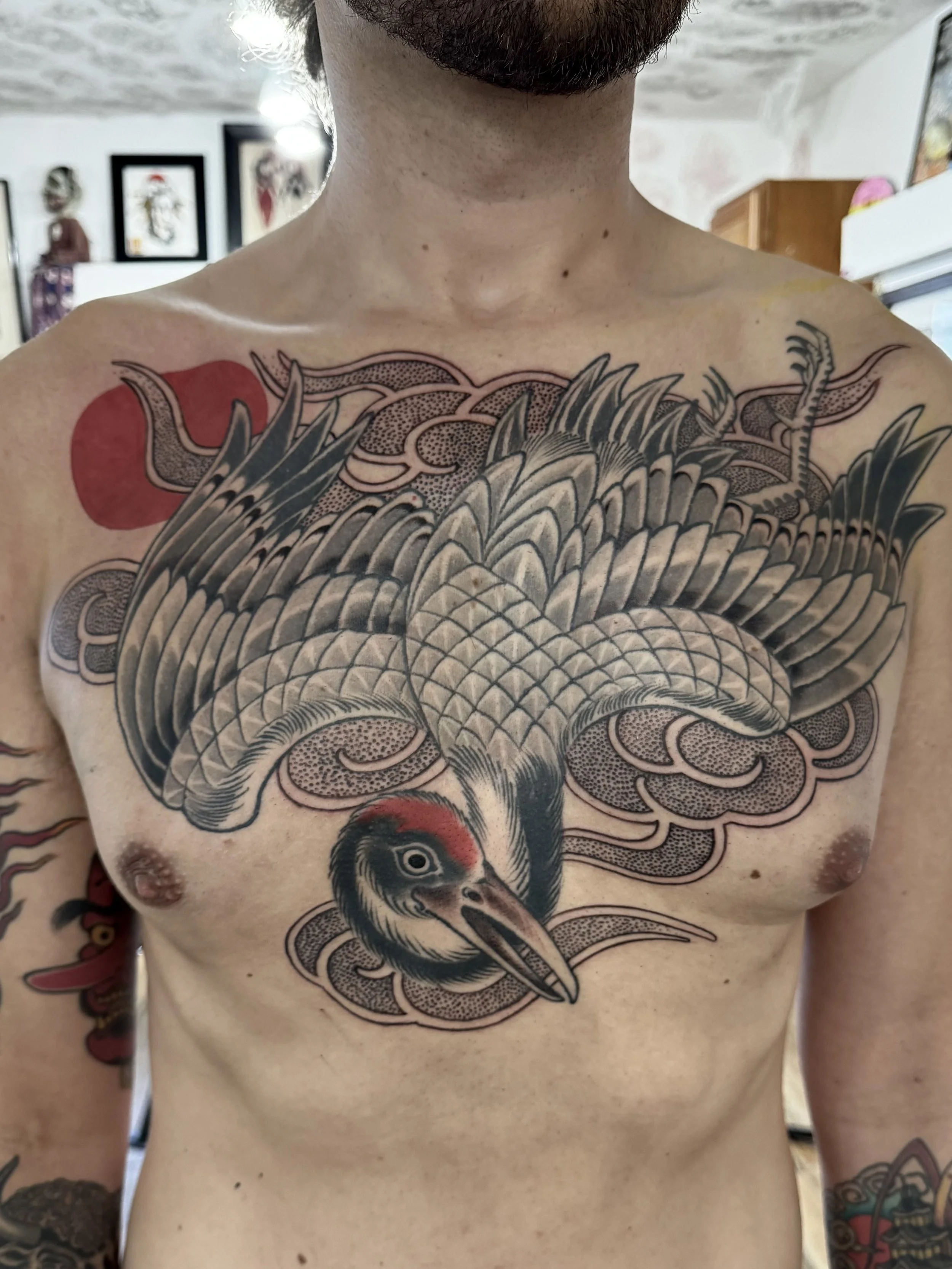 Tattoo of a large bird, likely a thunderbird, with detailed wings and head, surrounded by stylized clouds on a man's chest.
