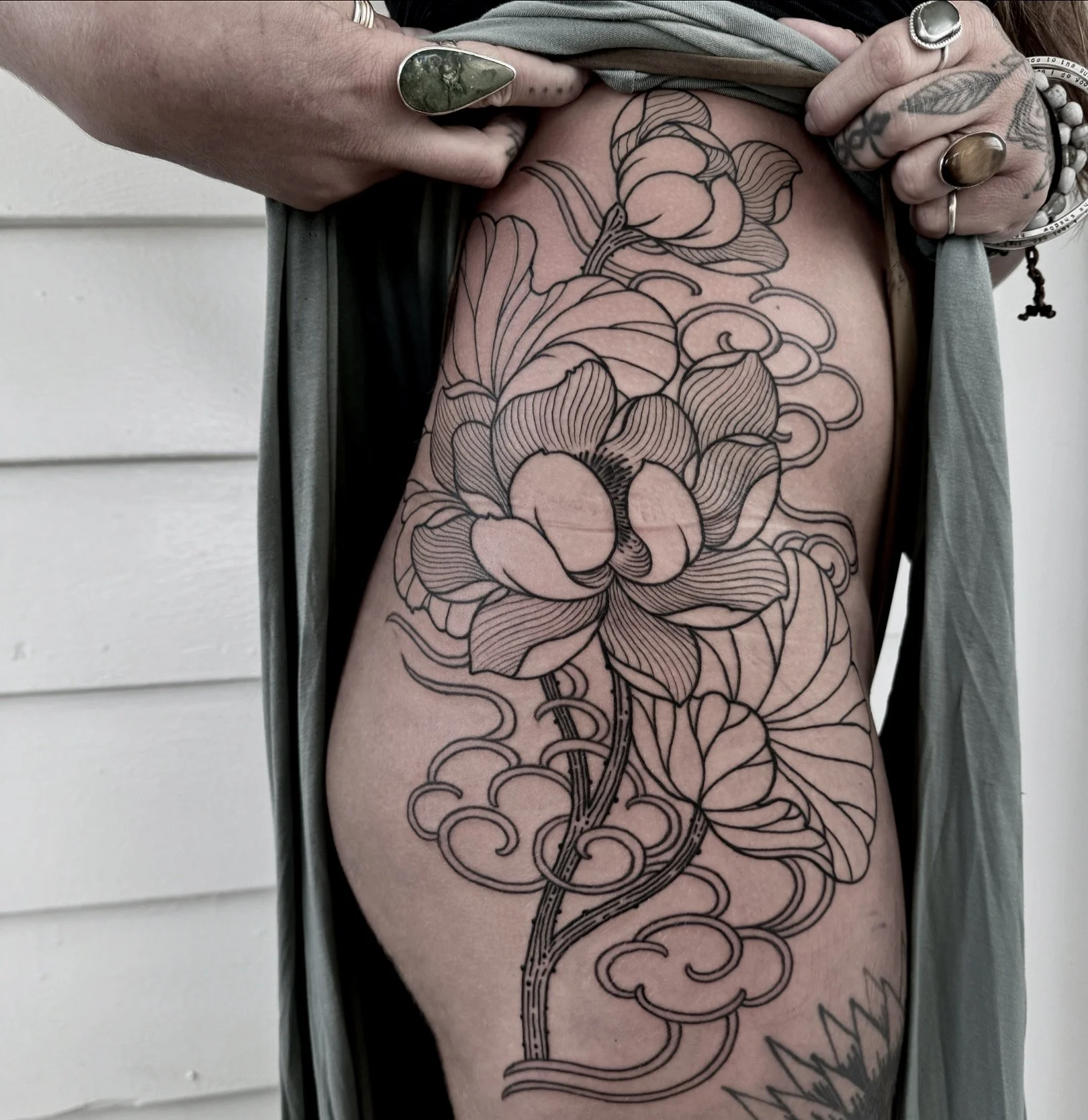 A person's side with a large, outlined floral tattoo featuring a detailed flower, leaves, and swirling patterns.