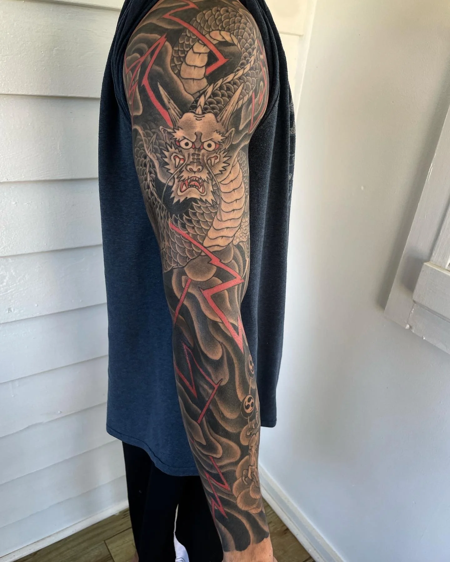 Tattoo of a fierce tiger with an open mouth and sharp teeth, surrounded by swirling clouds and red lightning bolts, on a person's arm.