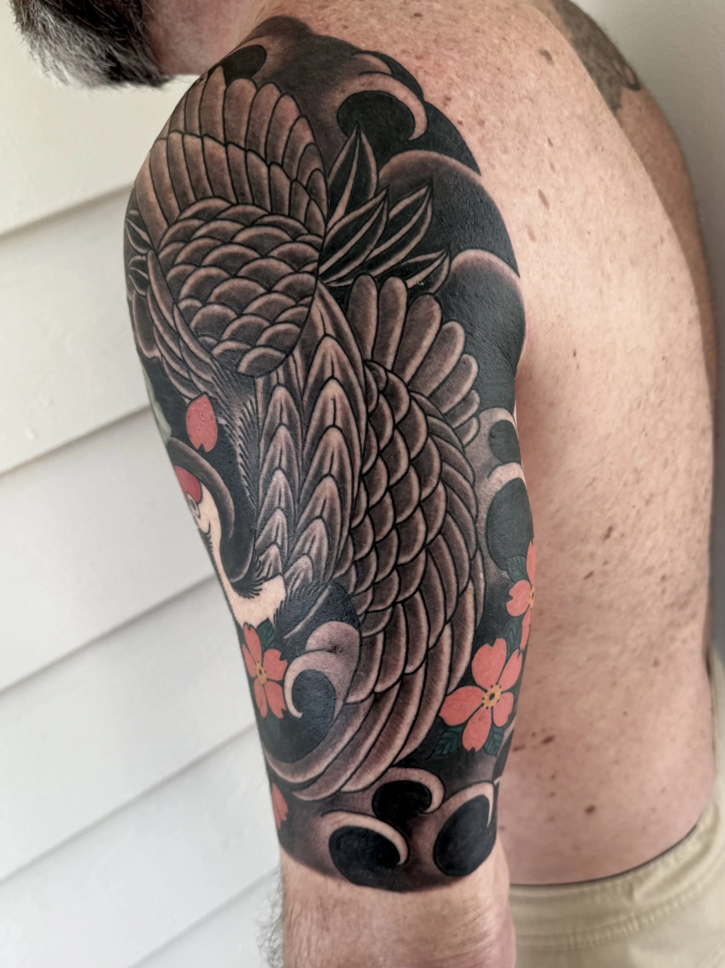 Tattoo of a koi fish with orange flowers on a person's upper arm.