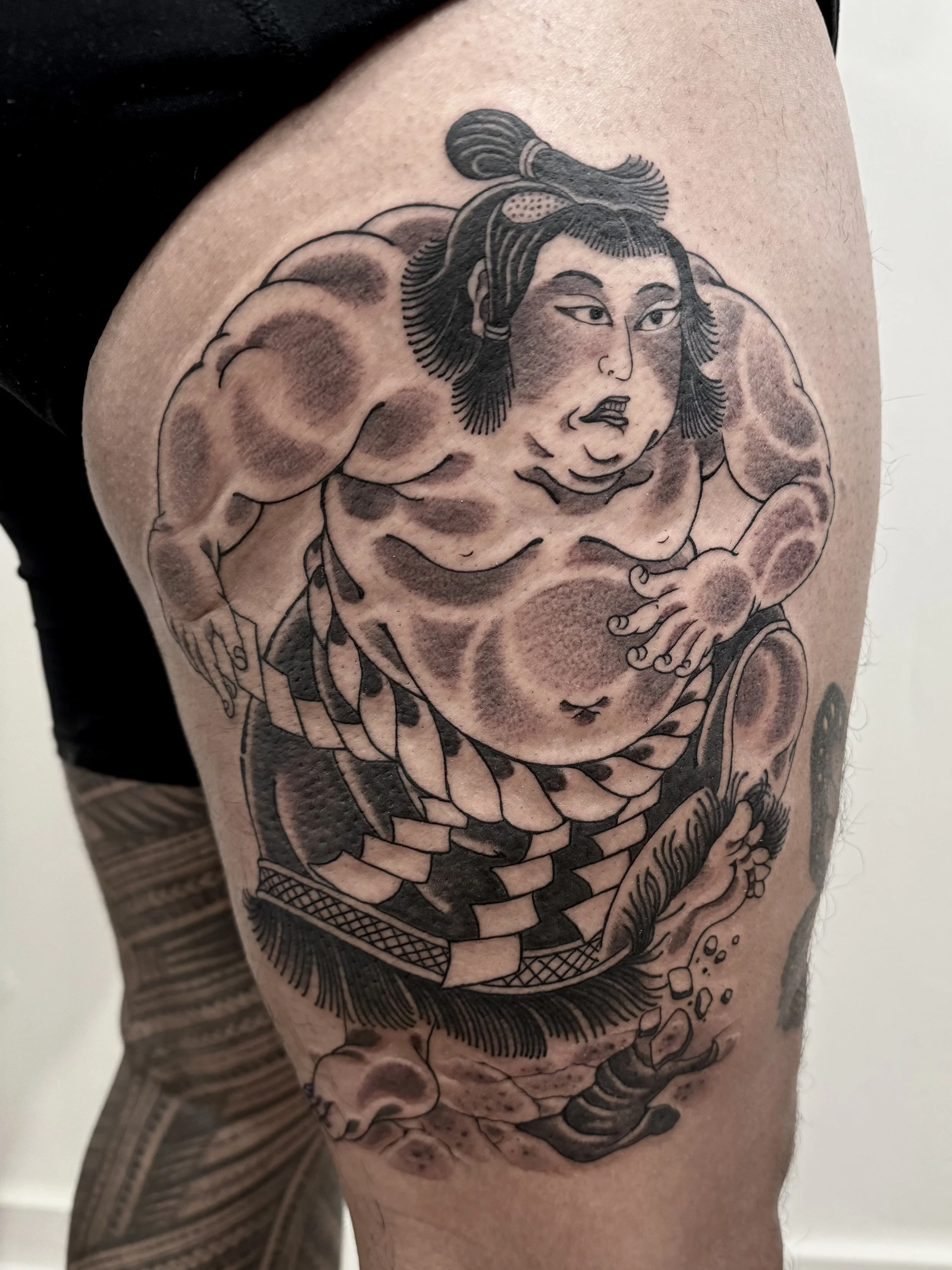 Tattoo of a sumo wrestler with a detailed facial expression, traditional hairstyle, and muscular body, depicted in a Japanese-style art design.