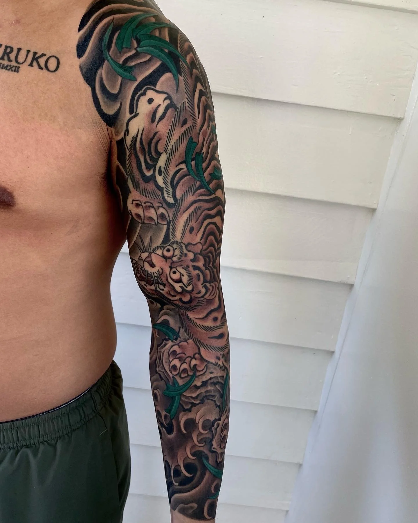 Tattoo sleeve featuring a tiger's face, clouds, teal leaves, and black and gray shading on a man's arm.
