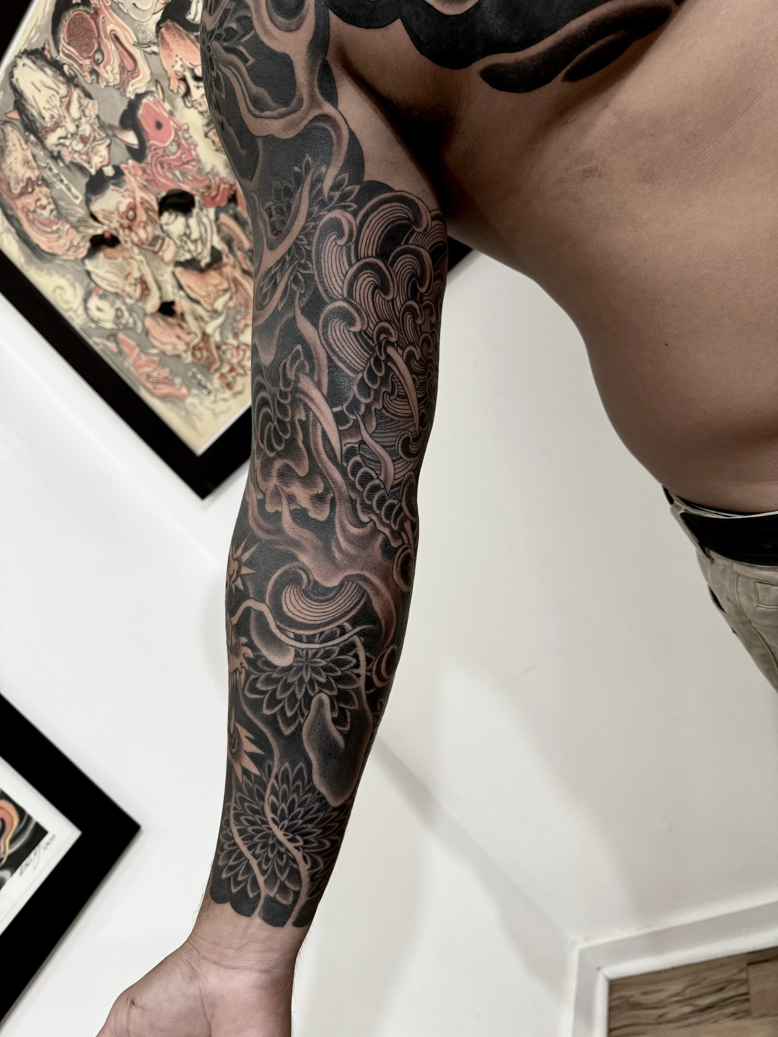 A person's arm with an elaborate black and gray tattoo sleeve featuring floral and abstract patterns.