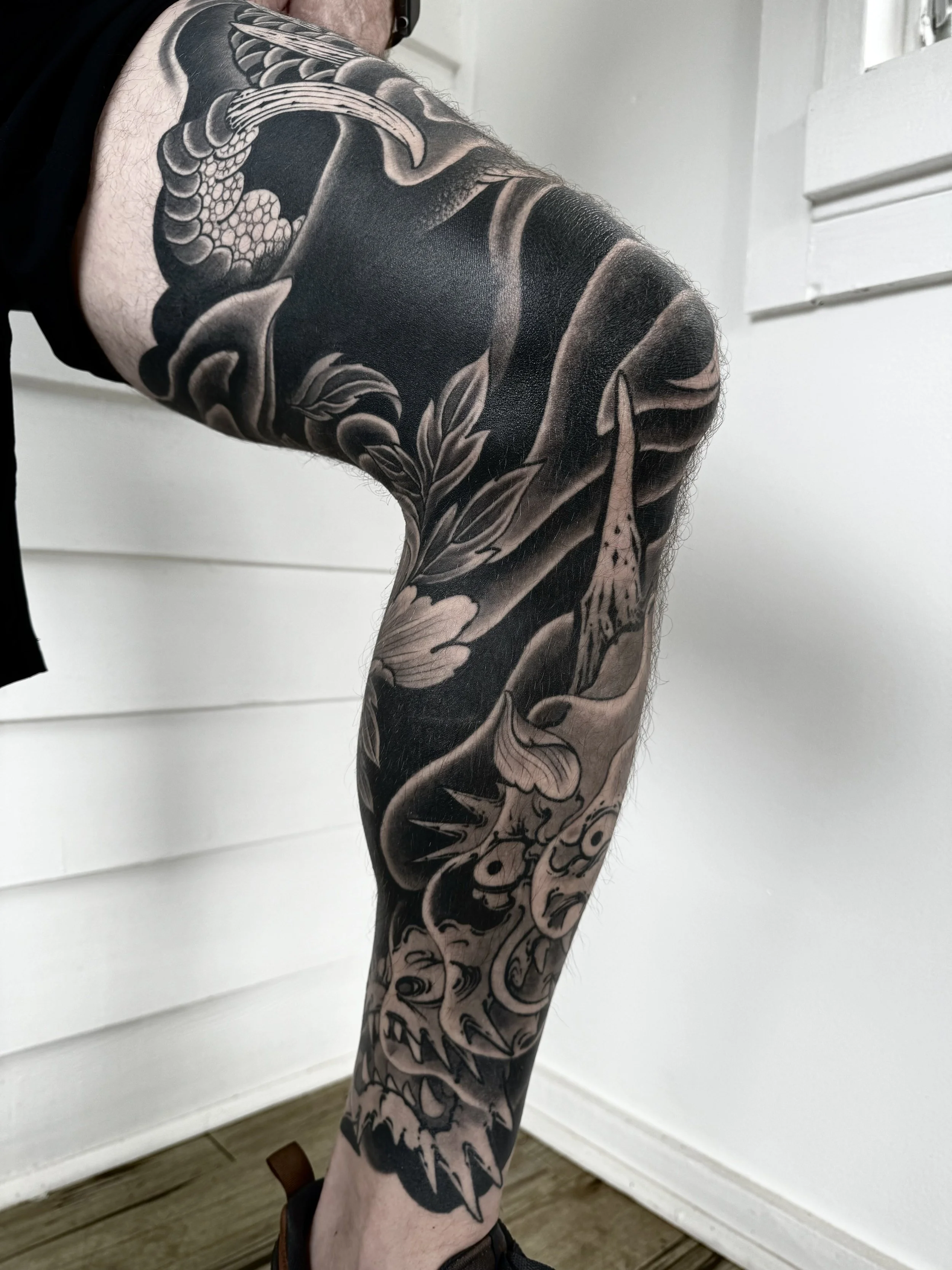 Close-up of a person's arm with a detailed black and gray tattoo featuring a snake, flowers, and a fearsome creature with sharp teeth.