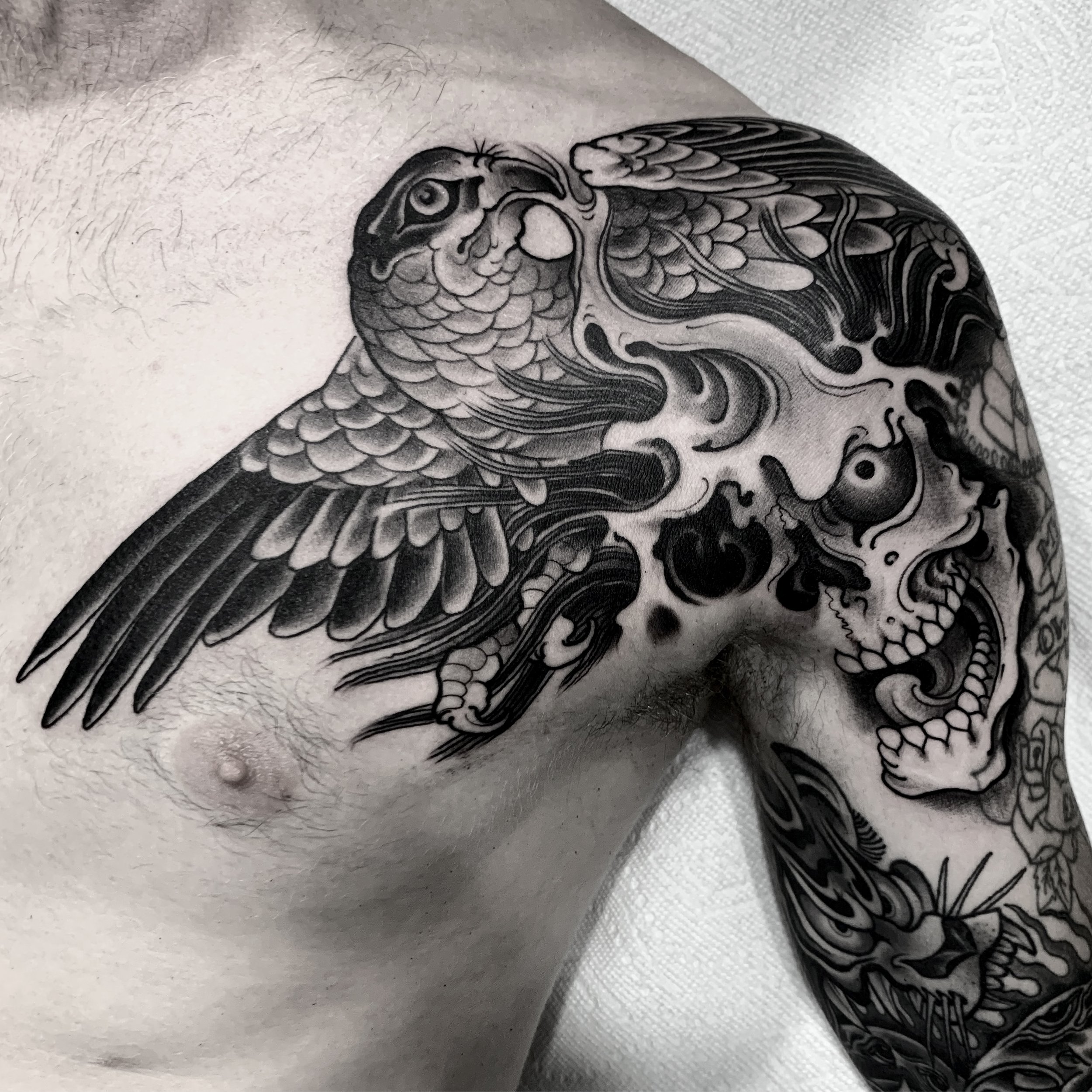 Black and gray tattoo of a bird with detailed feathers on a person's upper arm and shoulder, with turbulent lines and patterns surrounding the bird.