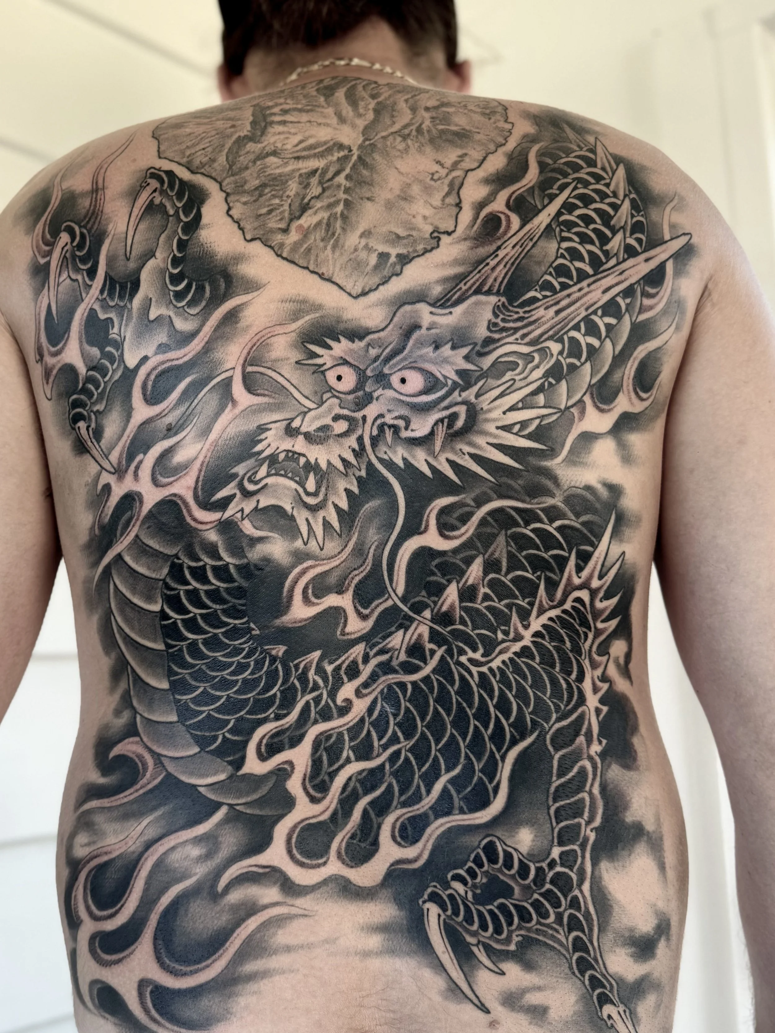 Black and gray Japanese-style dragon tattoo covering the back with clouds, scales, and a fierce expression.