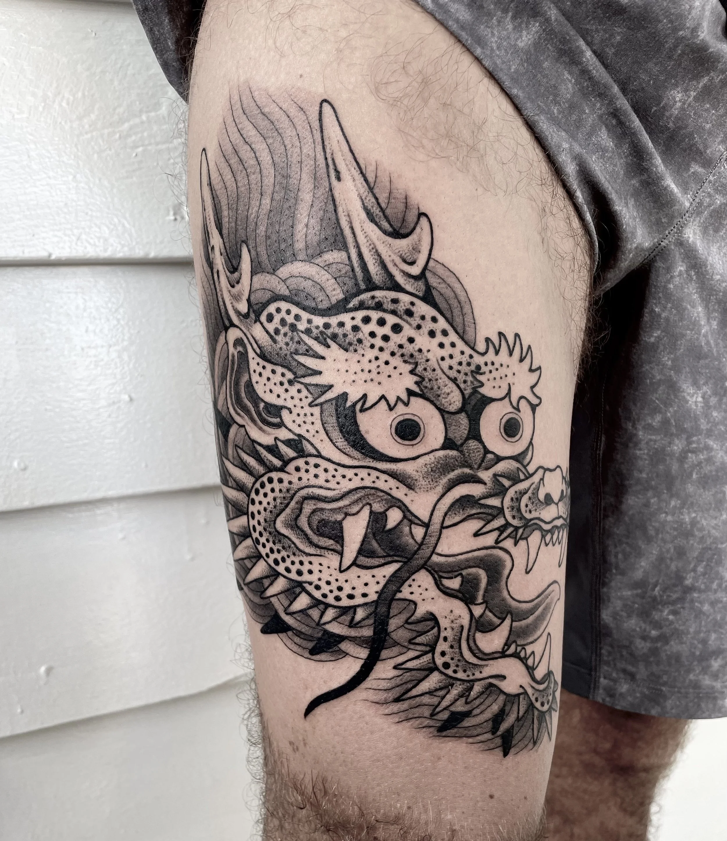 Black and gray tattoo of a traditional Asian-style dragon on a person's upper arm.