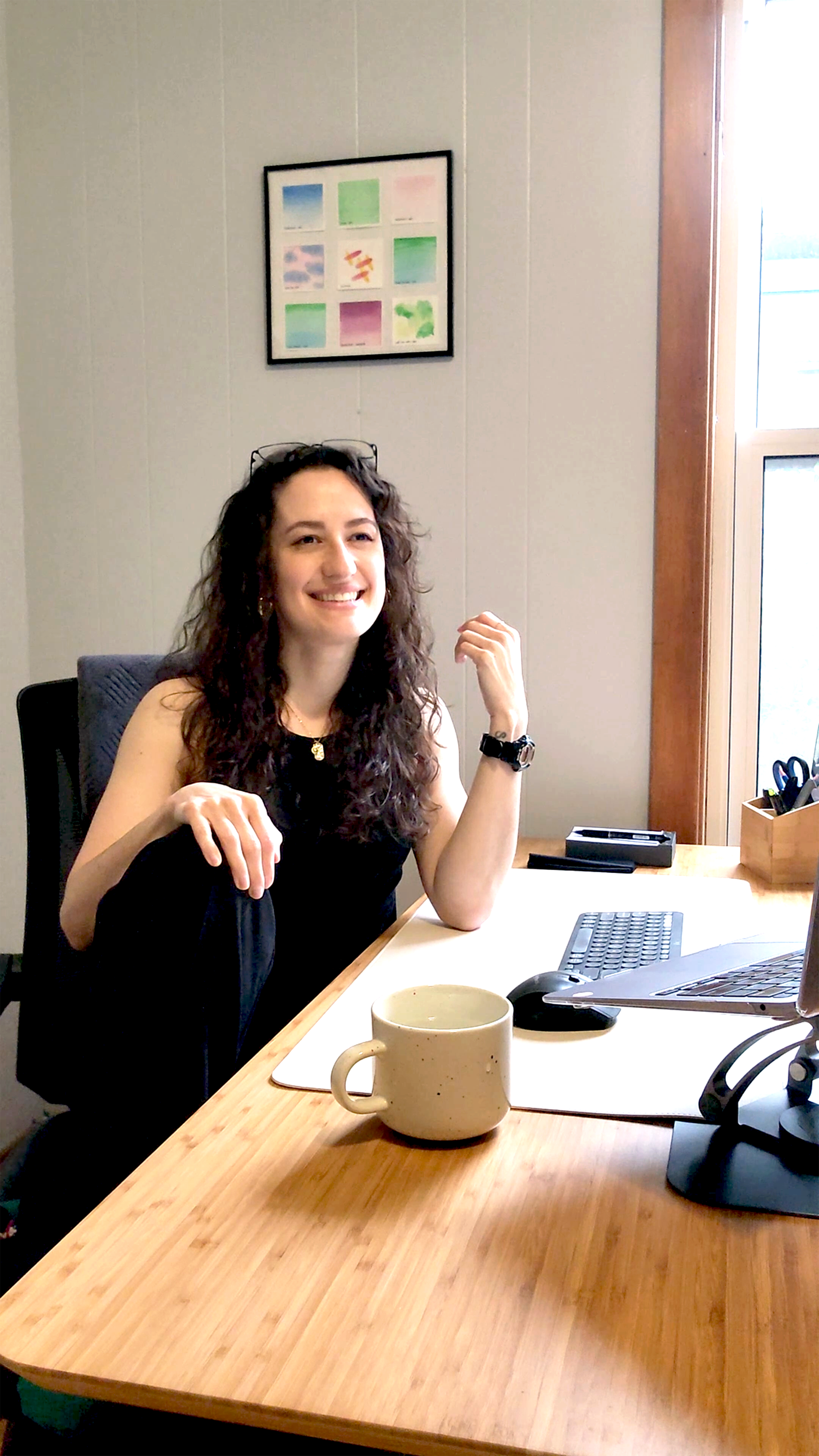 smiling woman with curly hair sitting at desk with cup and computer