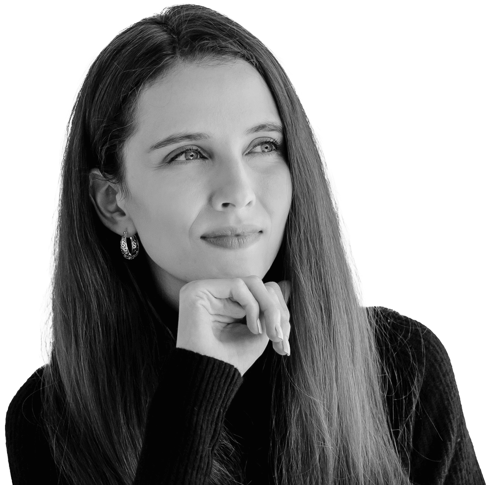 A woman with long hair and earrings, looking thoughtfully to the side with her chin resting on her hand, in black and white.