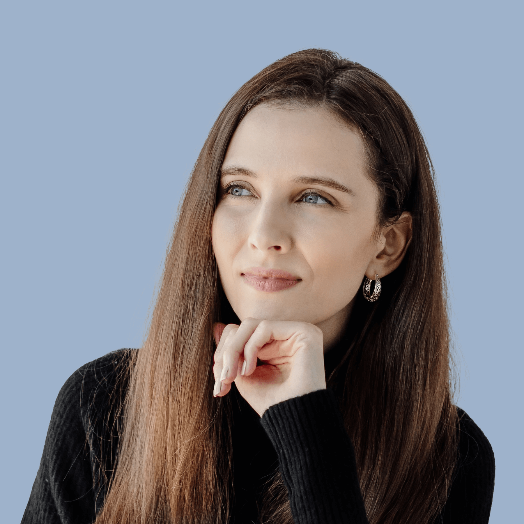 A woman with long brown hair, wearing a black sweater and silver hoop earrings, is resting her chin on her hand and looking thoughtfully to the side against a light blue background.