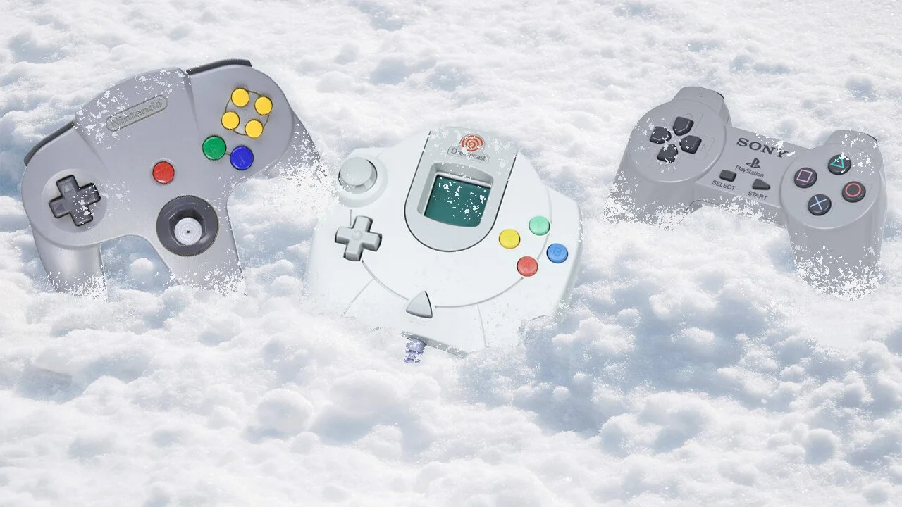Three retro gaming controllers partially buried in the winter snow, representing Nintendo, Dreamcast, and PlayStation