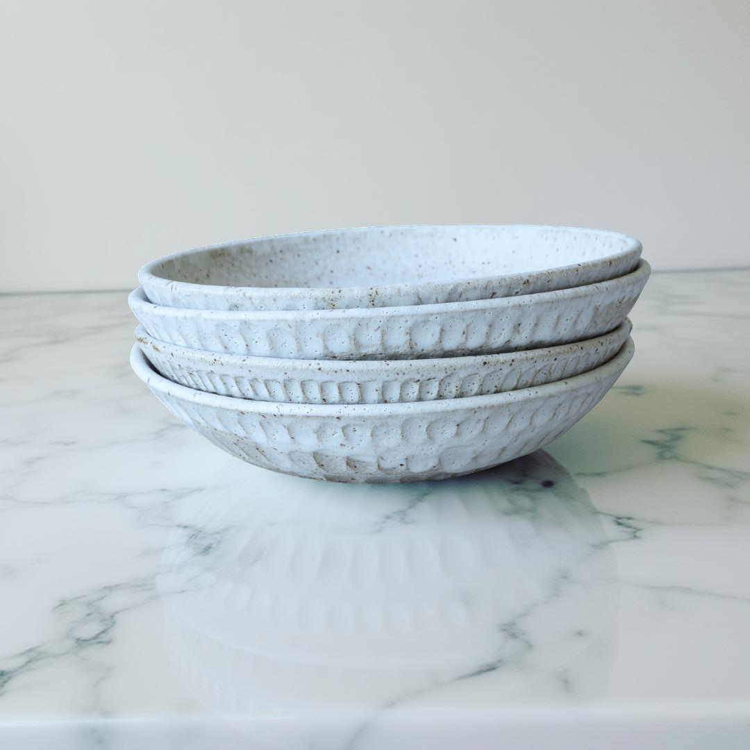 stack of textured fluted bowls in a greay speckled glaze, sitting on top of a marble counter with plain background