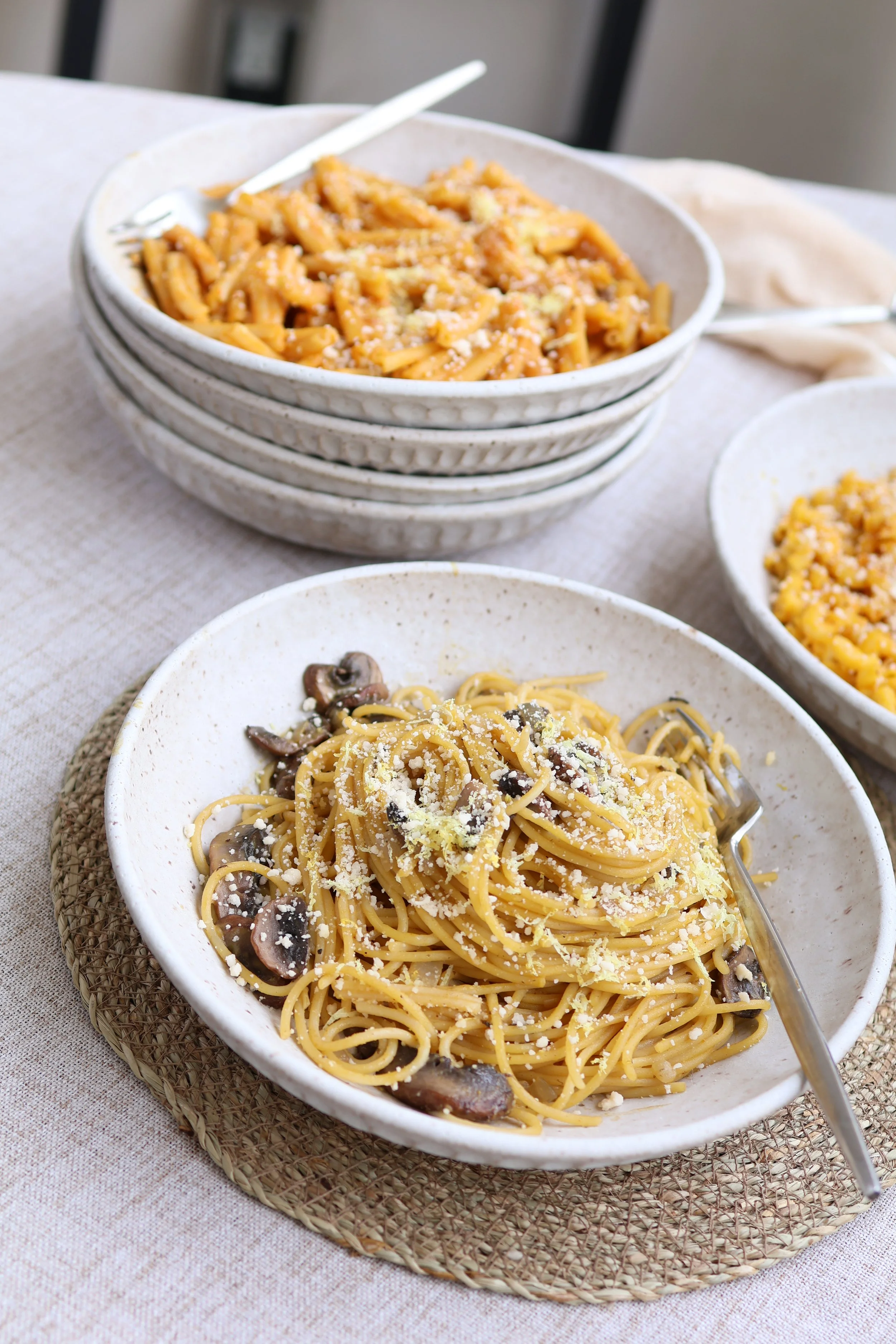 Bowls of pasta dishes with grated cheese, one with spaghetti and mushroom, another with a creamy sauce and pasta.