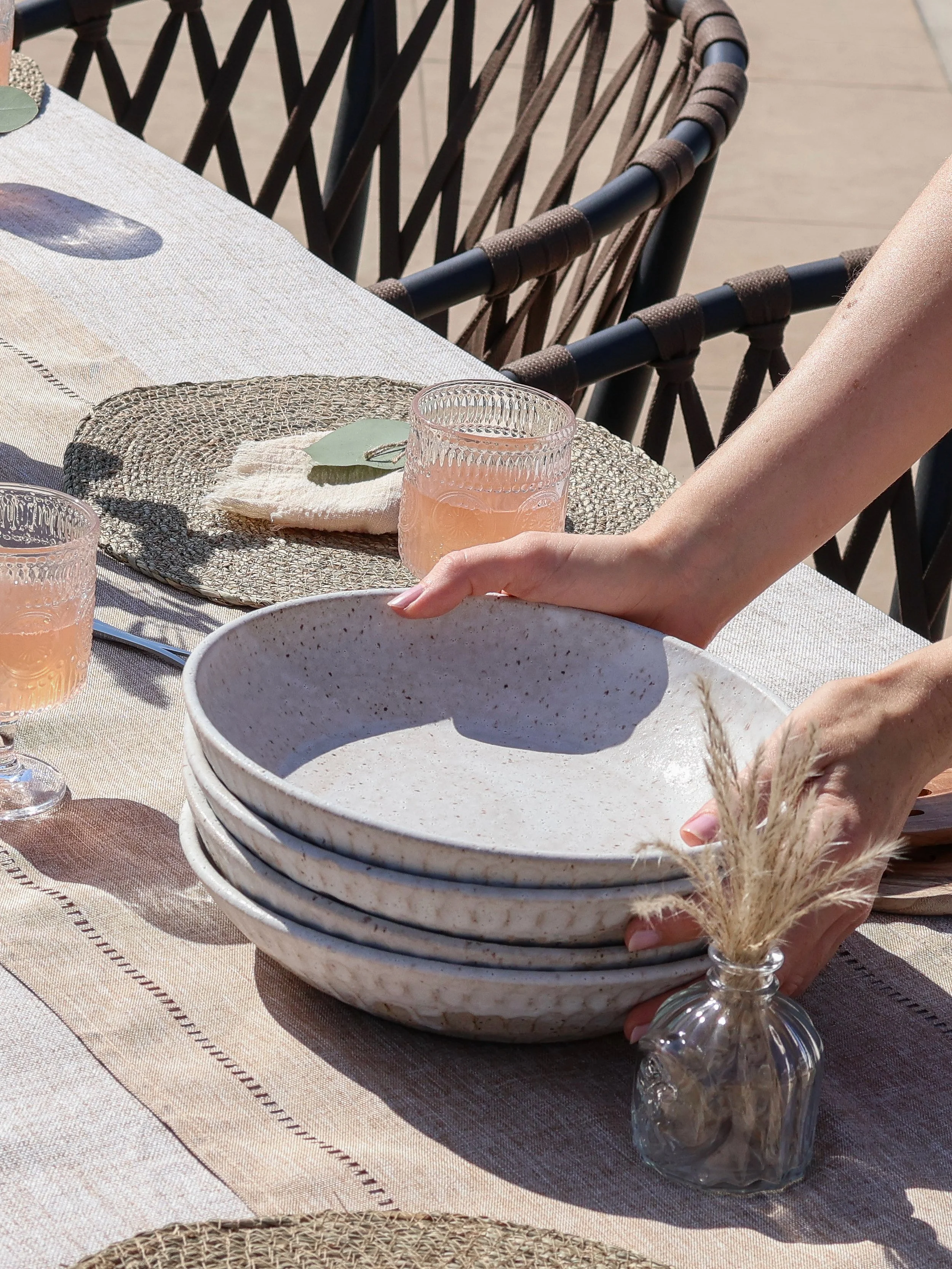 hands picking up the textured bowl on a table with two glasses of pink wine and a glass vase with natural ferns as decoration