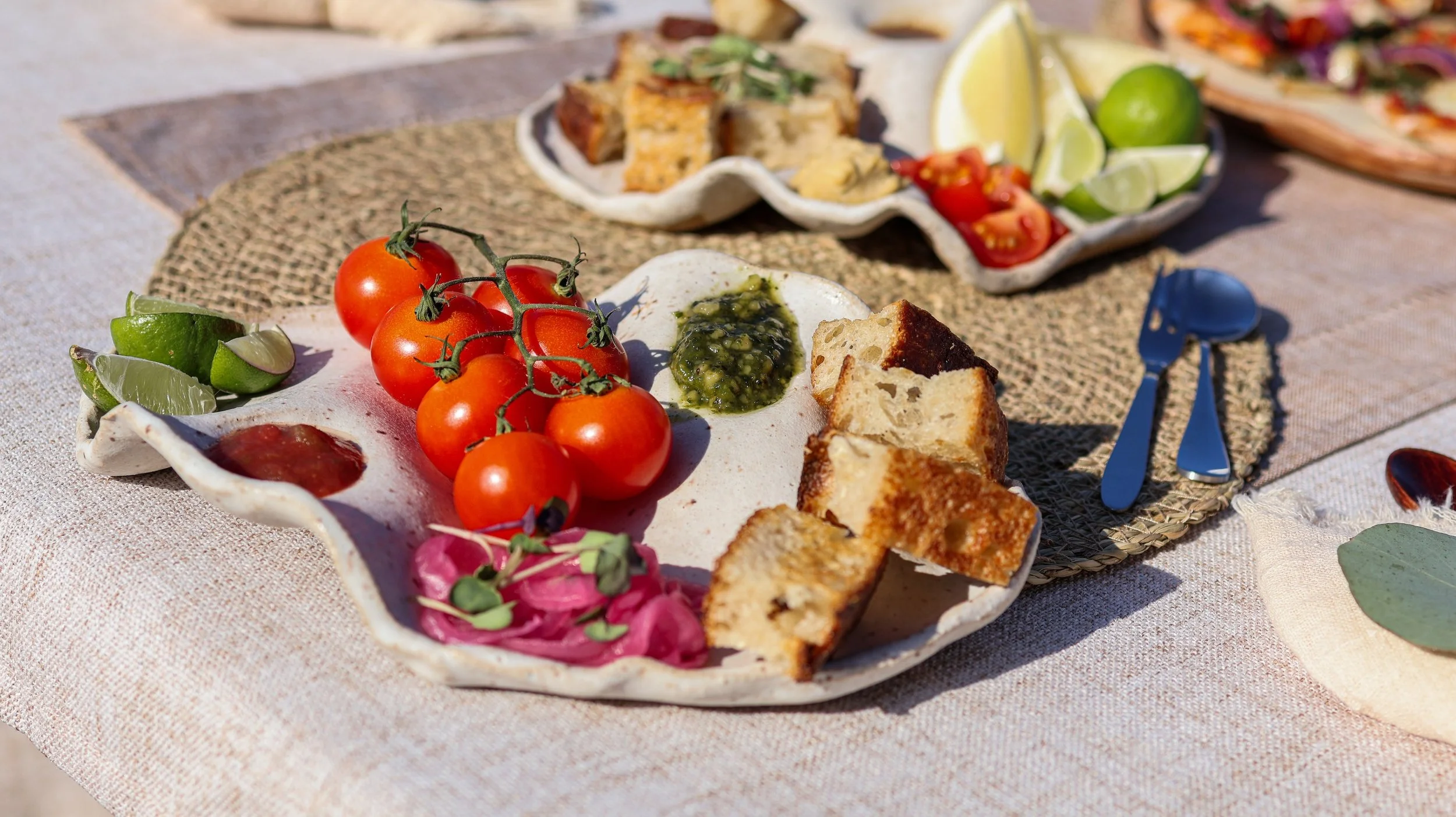 A ceramic serving platter with cherry tomatoes, lime wedges, green sauce, and toasted bread.