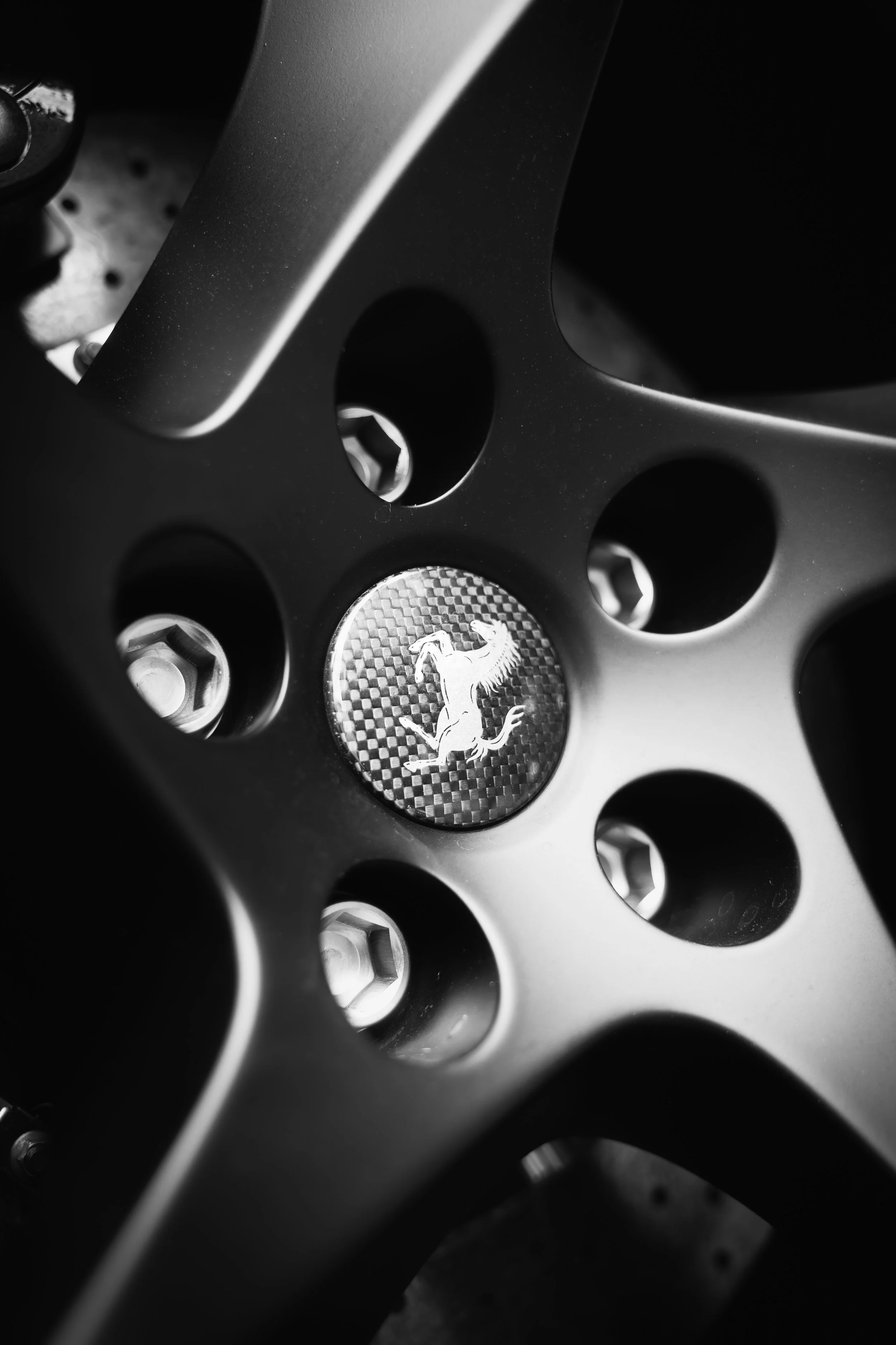 Close-up of a Ferrari wheel with a prancing horse emblem in the center, black and white photo.