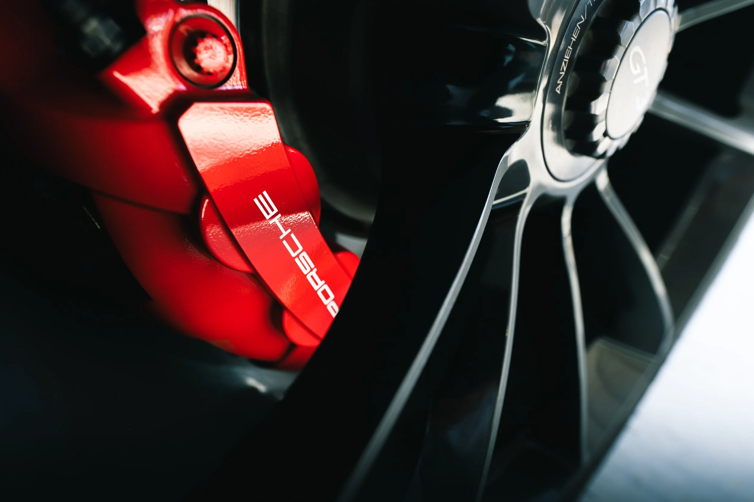 Close-up of a black and silver Porsche GT wheel with a red brake caliper that has the Porsche logo on it.