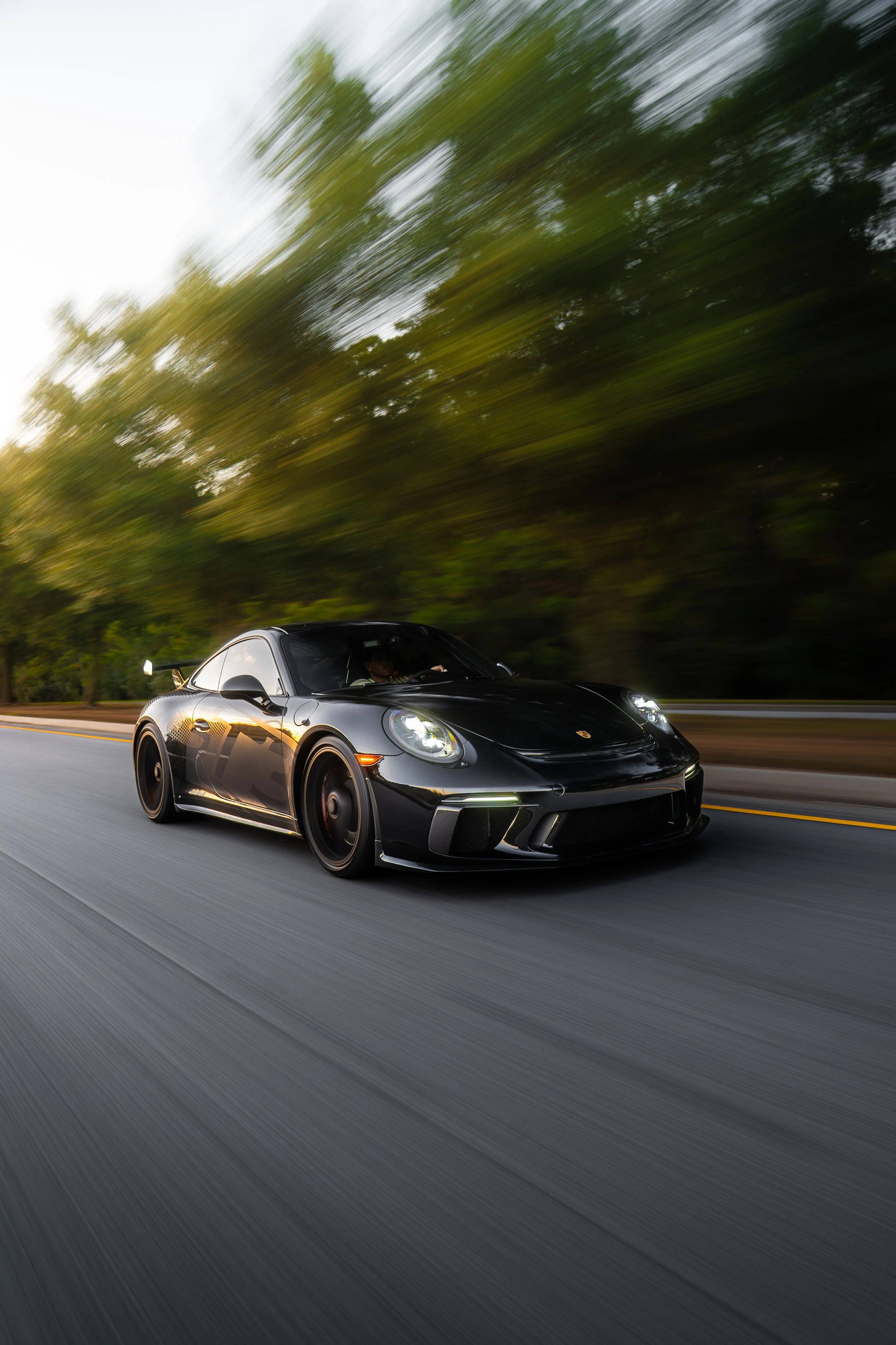 A black sports car driving on a highway through a blurred green and gray landscape.