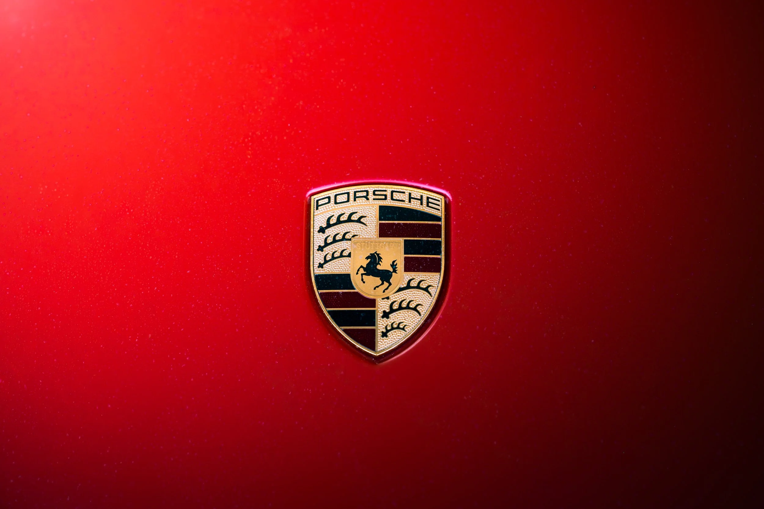 Close-up of the Porsche logo on a red car with a glossy finish.