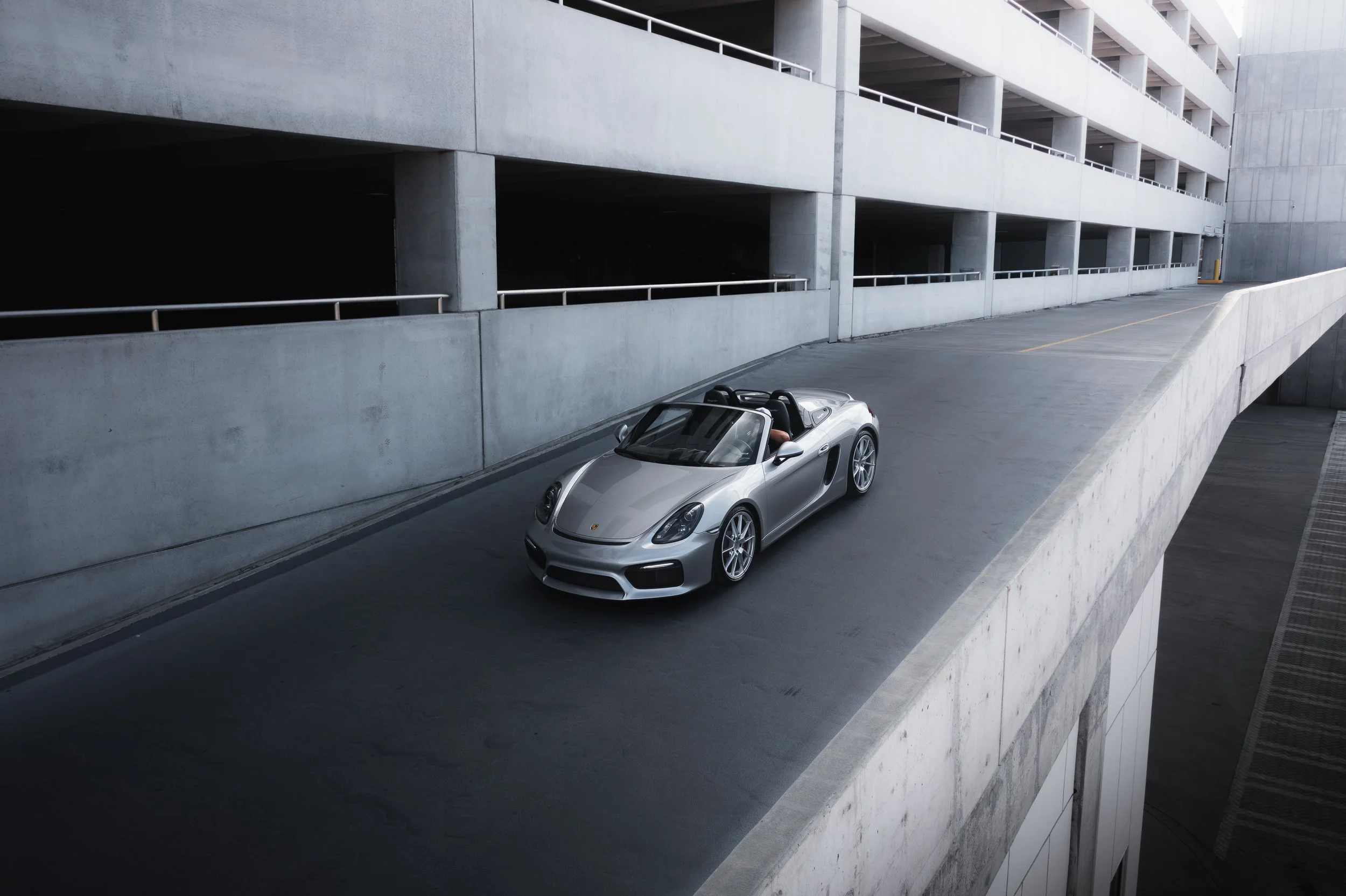A silver convertible sports car parked on a ramp in a concrete multi-level parking garage.