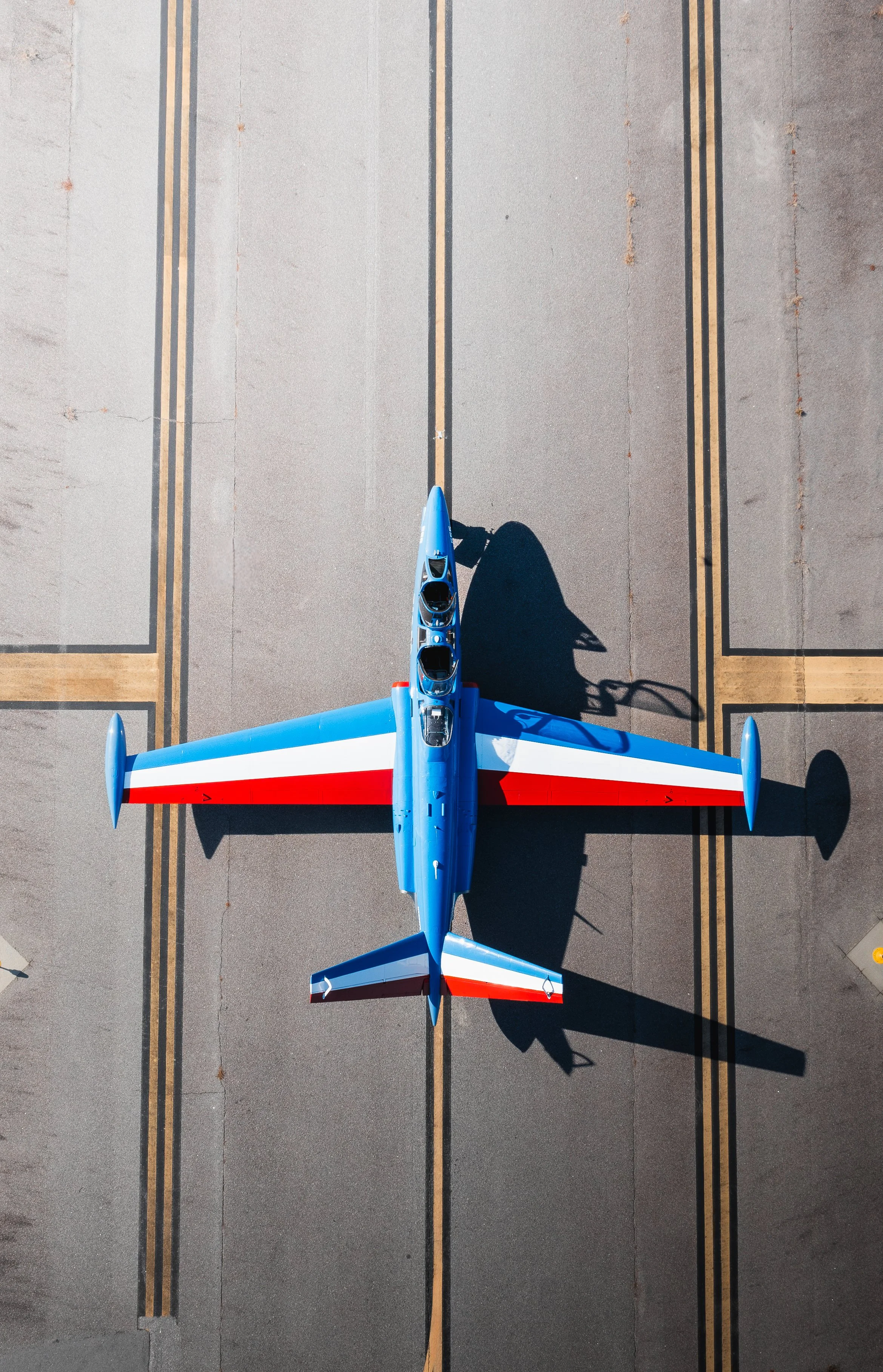 Colorful jet aircraft painted in blue, white, and red, viewed from above on tarmac.
