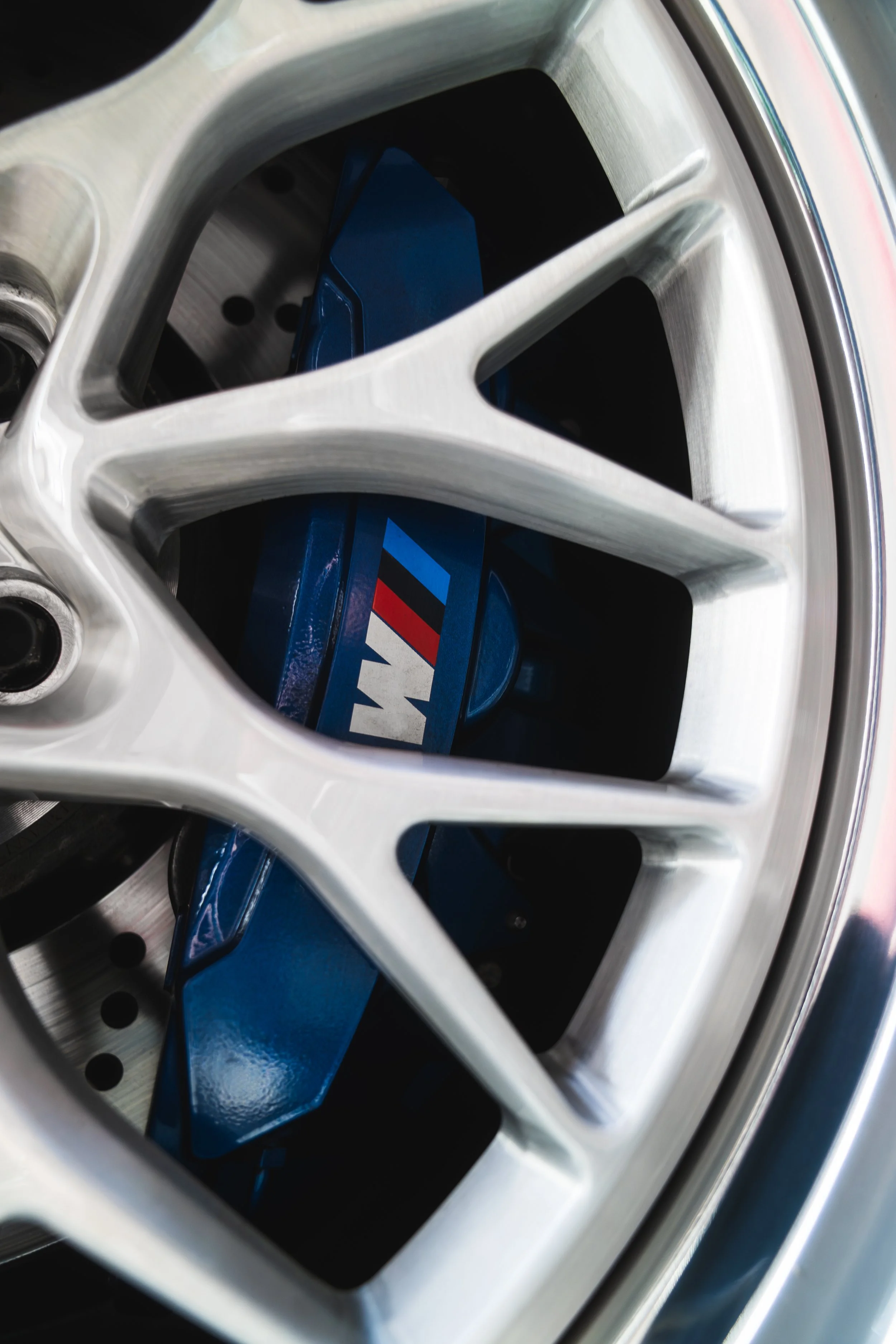 Close-up view of a car wheel with a silver alloy rim and a brake caliper painted in blue with BMW M logo.