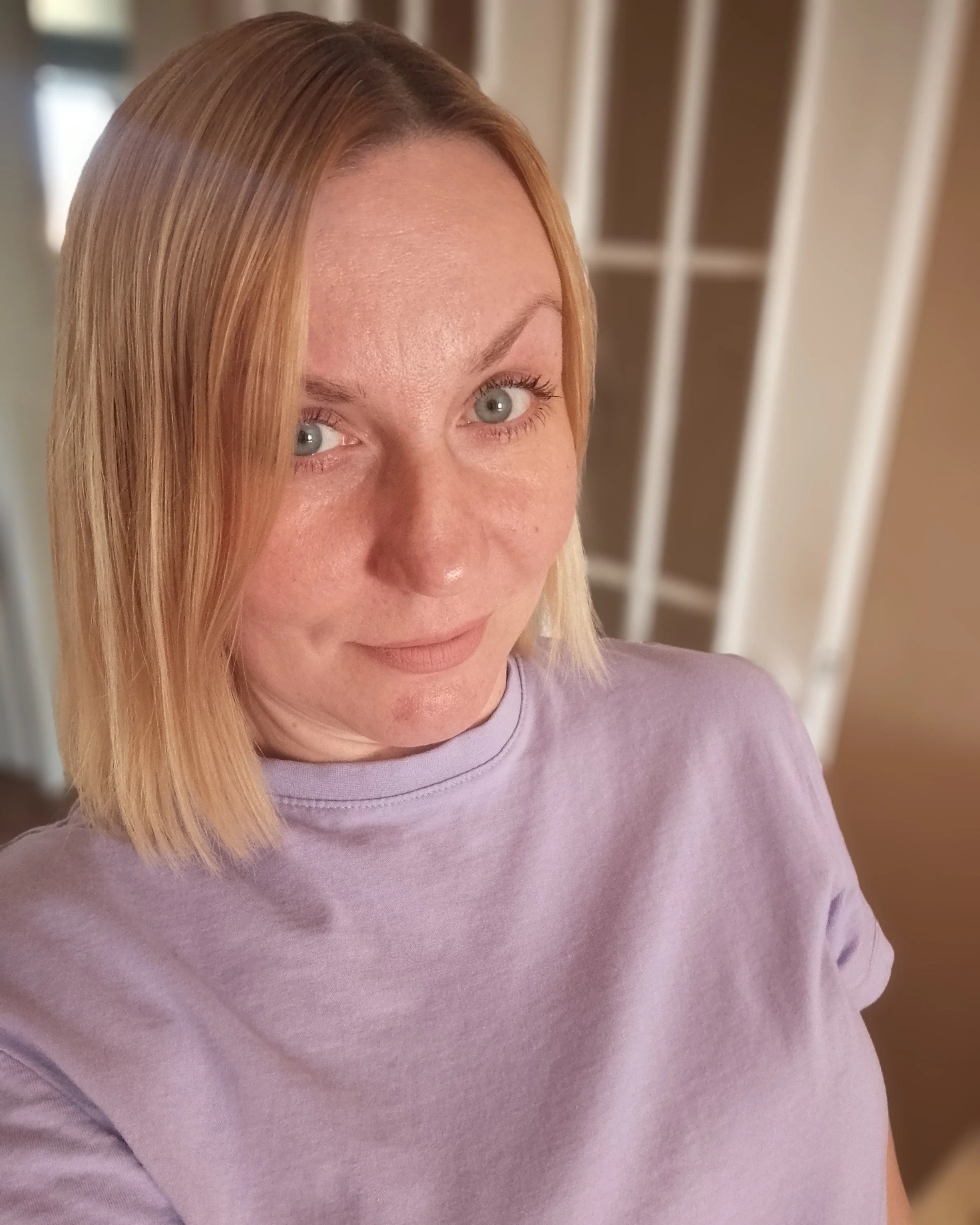 A woman with blonde hair wearing a lavendar colored shirt. 