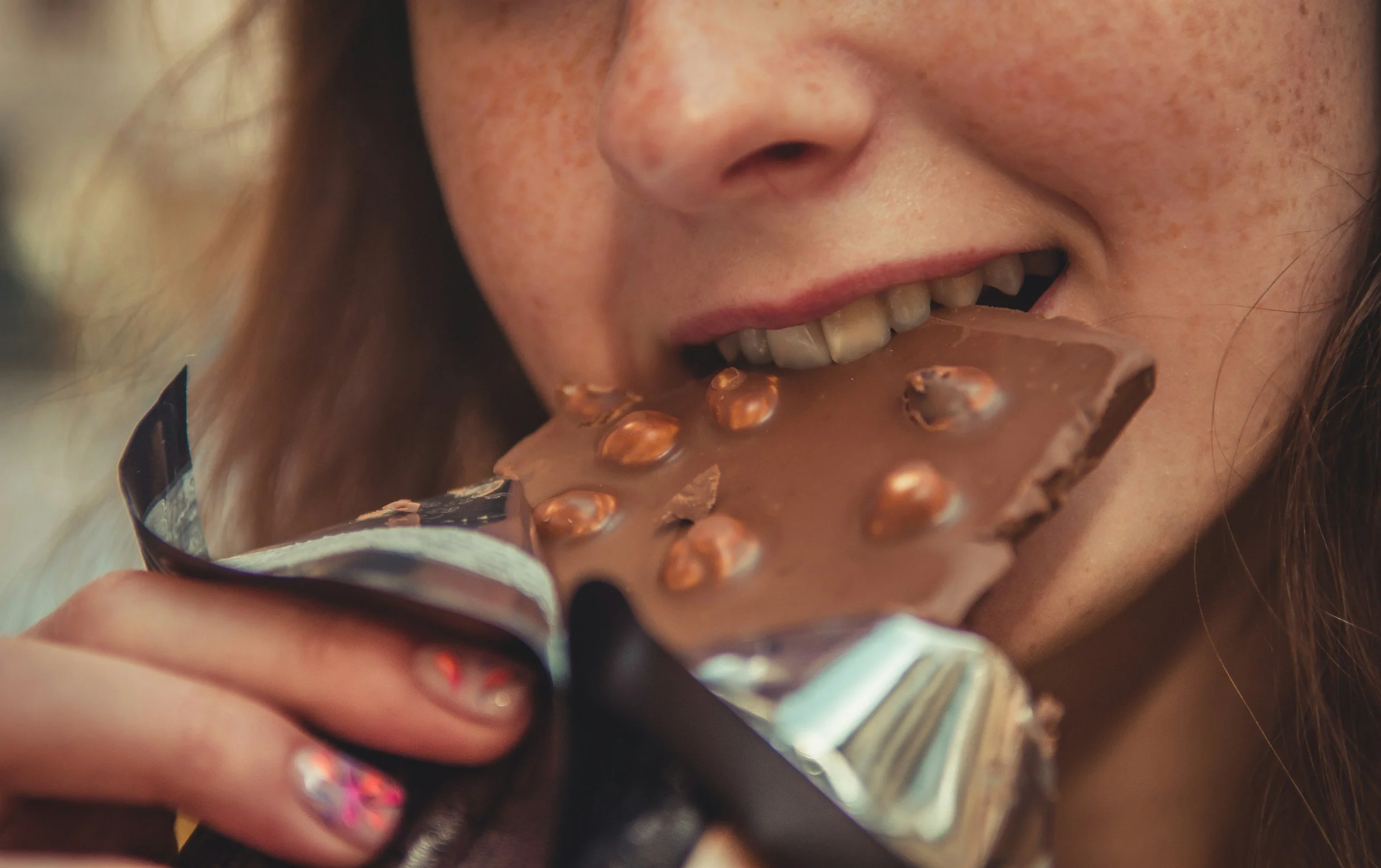Person biting into a chocolate bar, representing food cravings and finding peace with eating