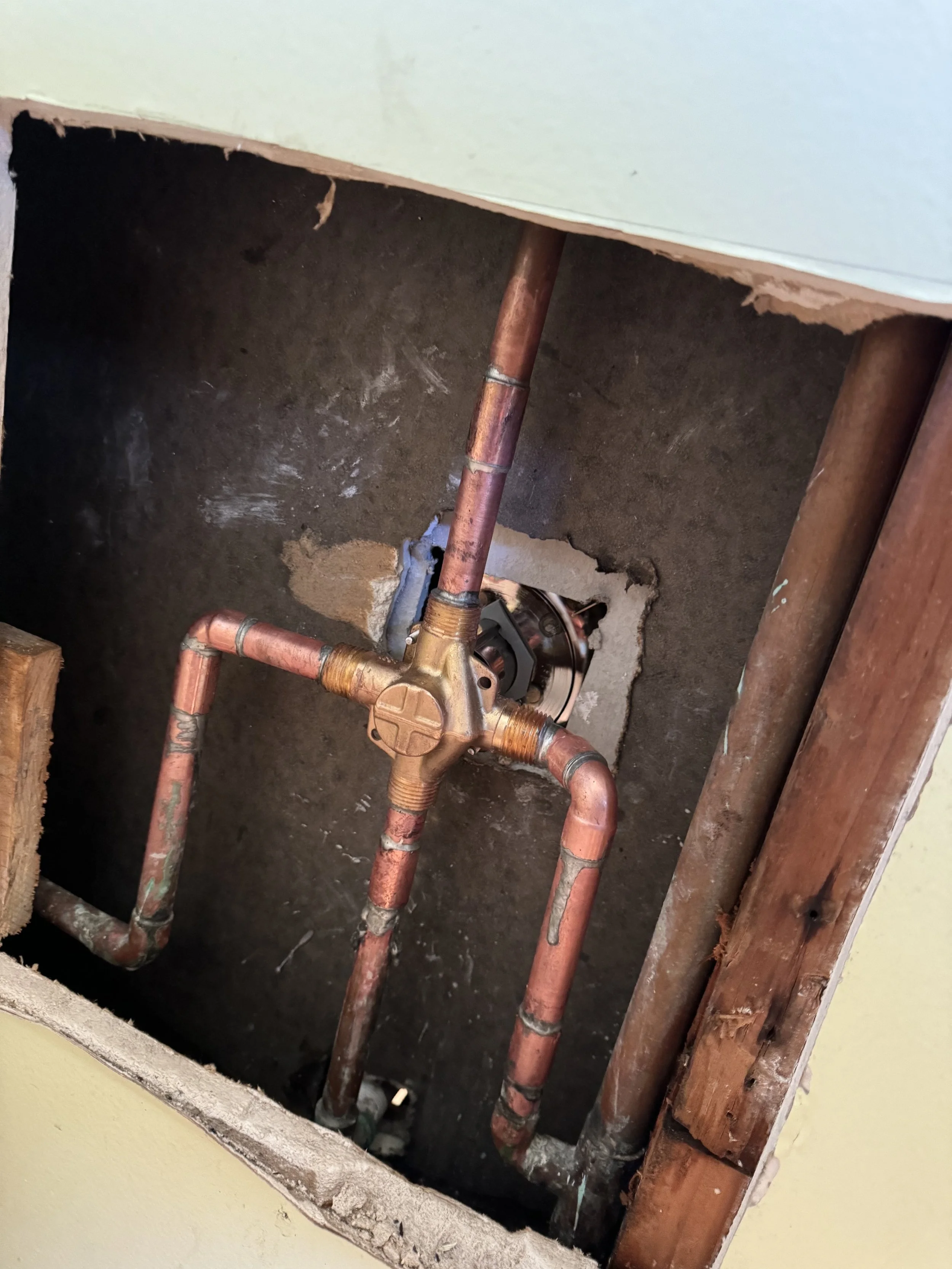 Copper plumbing pipes installed in a wall, with a valve and pipe connections visible.
