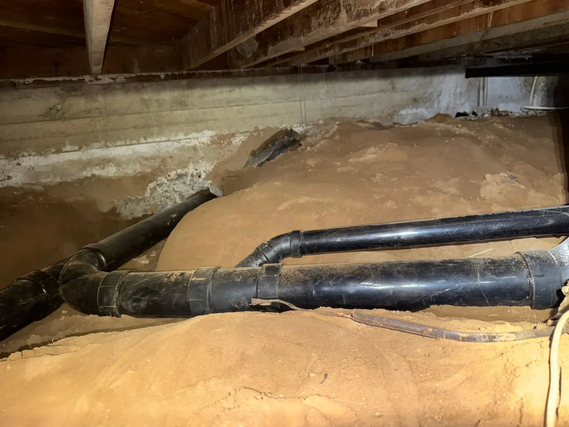 Underground plumbing pipes and dirt in a crawl space or basement area.