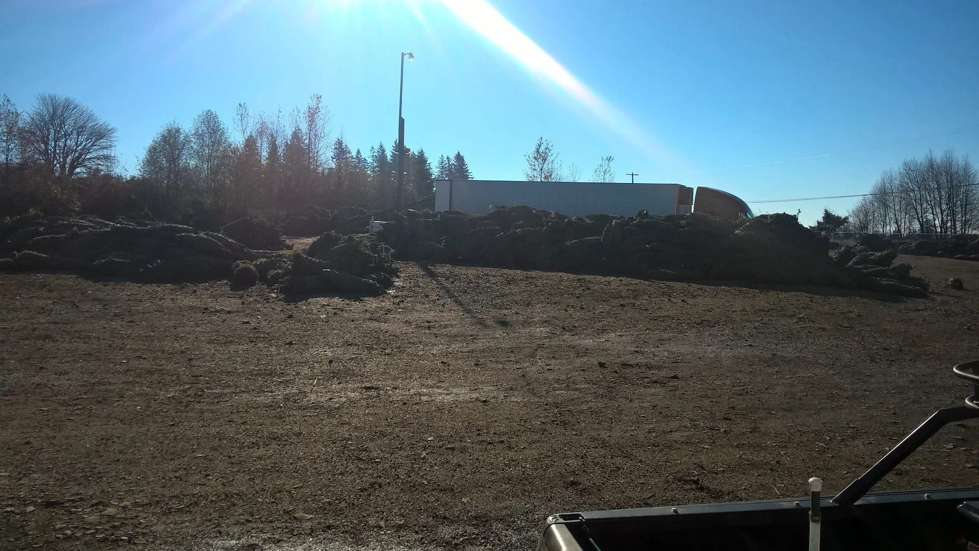Construction or landscaping site with dirt ground, large rocks, and a white semi-truck in the background under a clear blue sky with sunlight shining down.