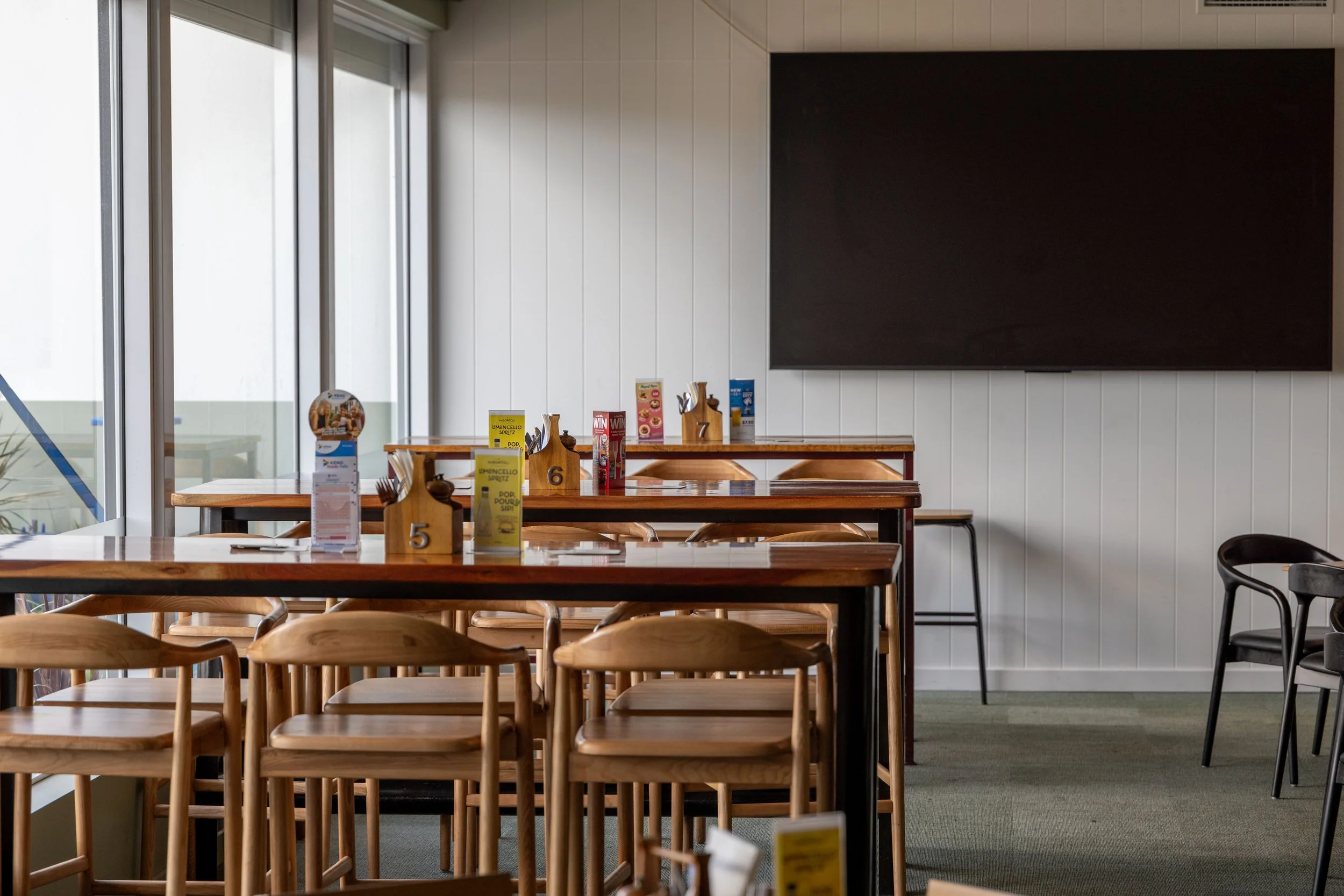 Wooden tables with stool seating in a room with a large tv.