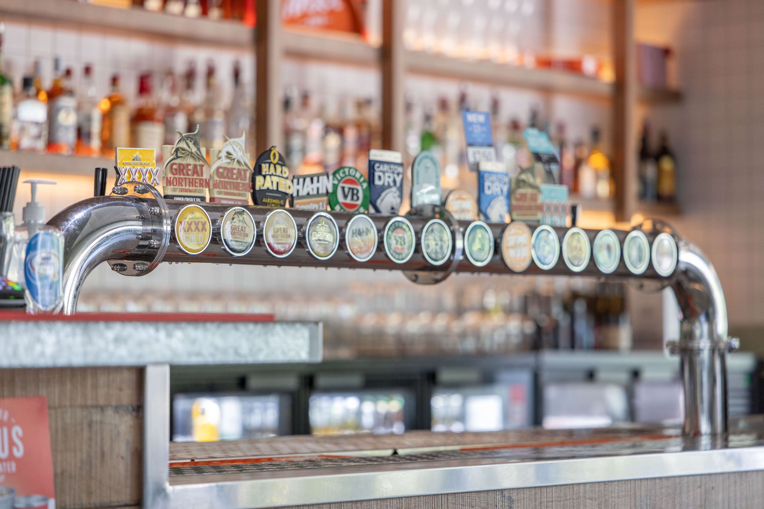 Beer tap handle with multiple beer labels in a bar.